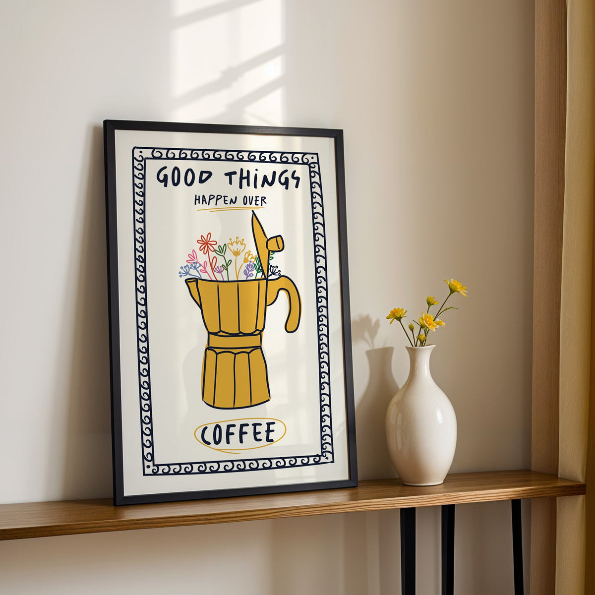 Good things happen over coffee print in a black frame on a console table with daisies