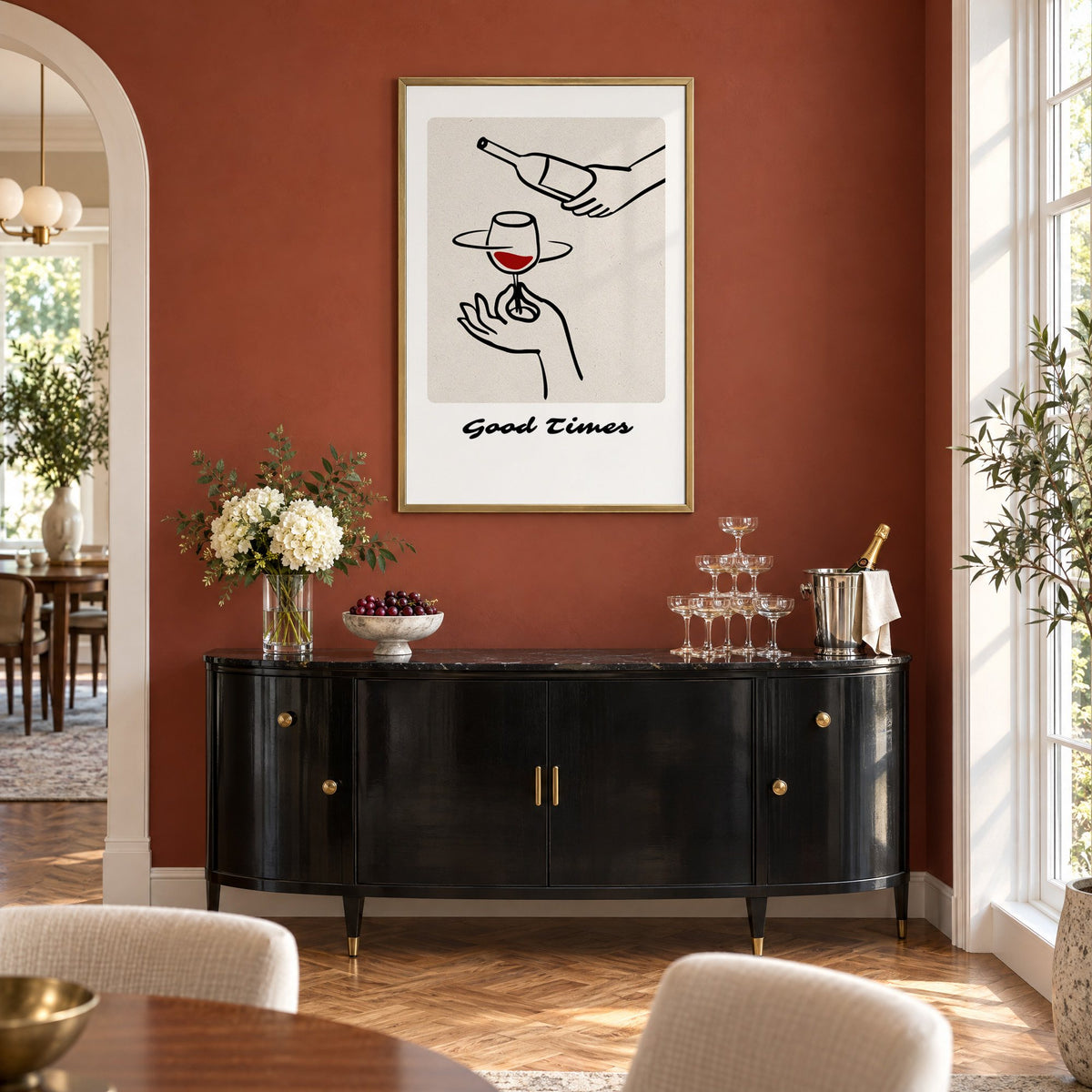 Good Times wine pour line art print in a brass frame on a terracotta wall above a black buffet with a champagne tower