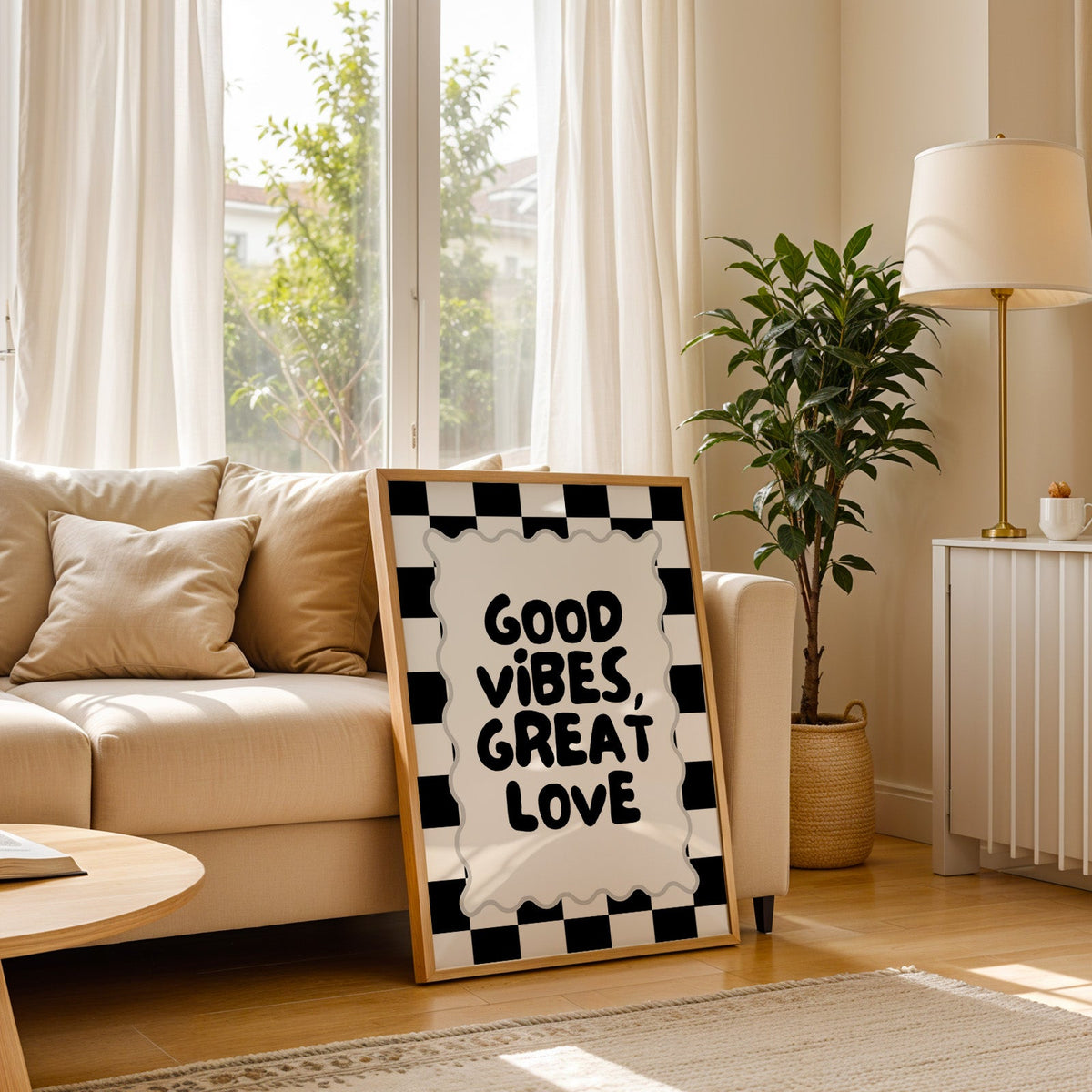 Good vibes great love checkerboard quote print in a light oak frame leaning on a cream sofa beside a floor lamp