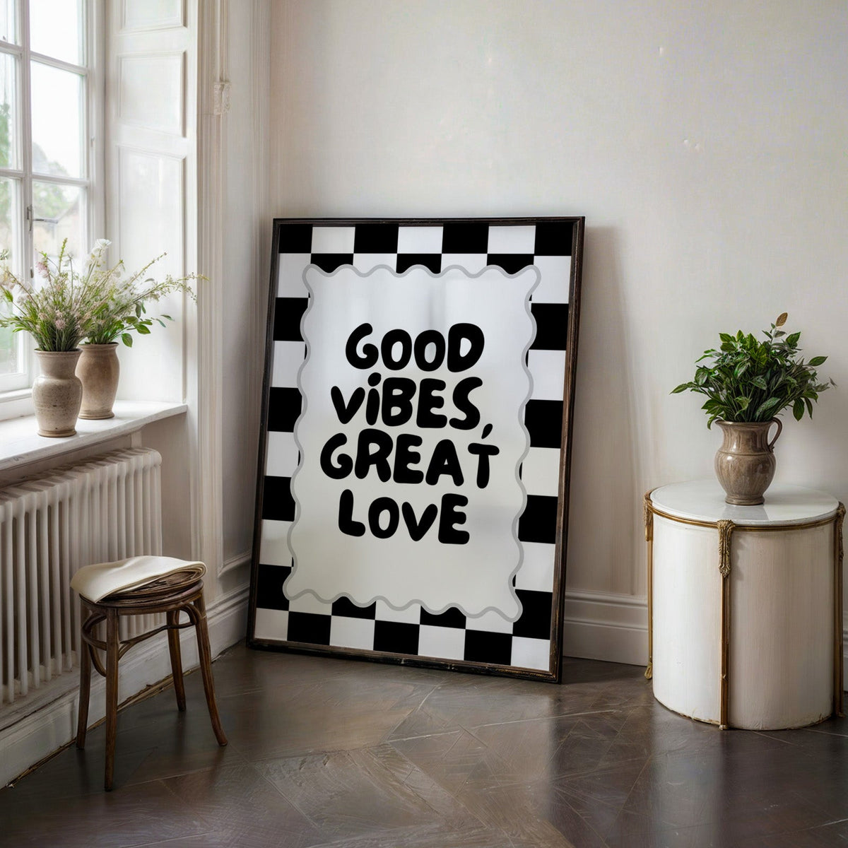 Good vibes great love checkerboard quote print in a black frame on a dark stone floor beside a white side table