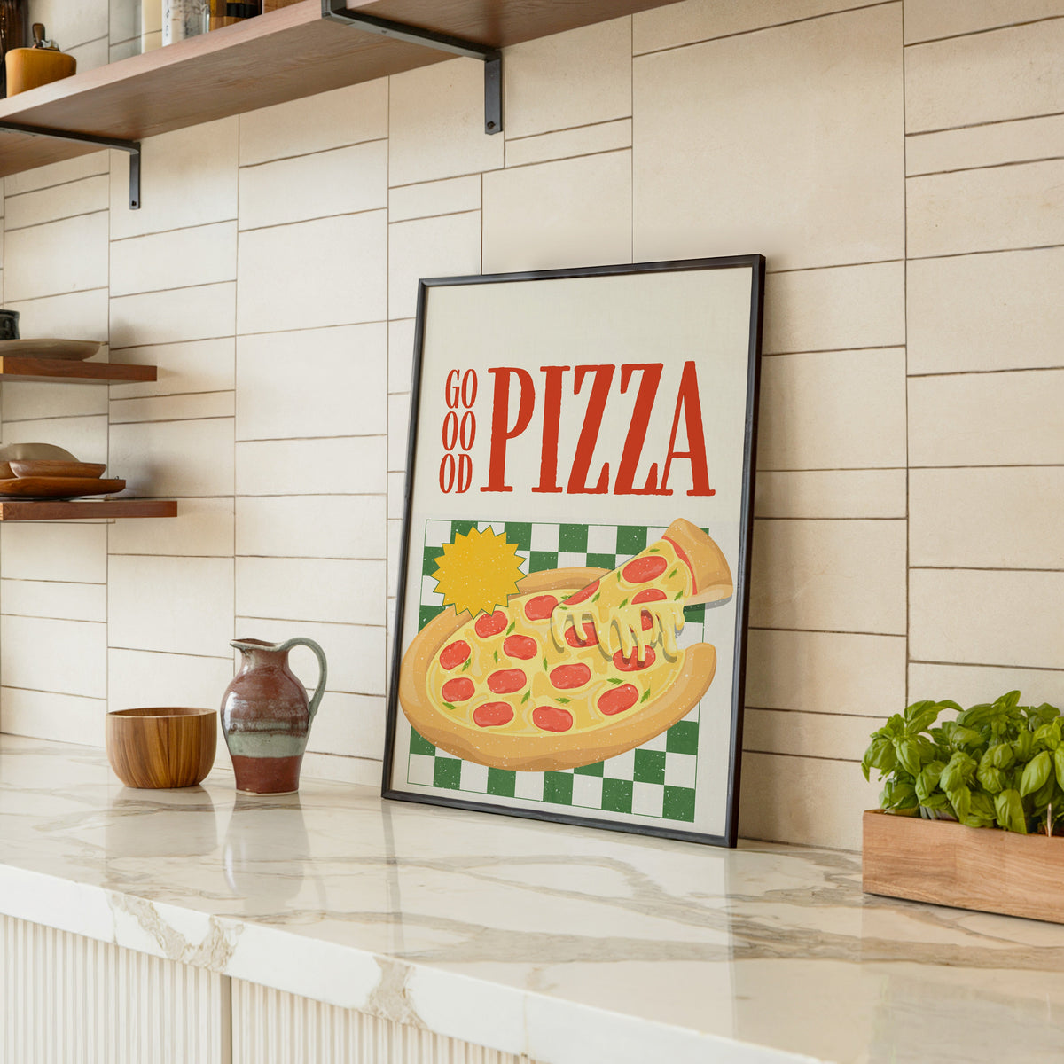 Goood Pizza print in a black frame leaning on a marble counter in a tiled kitchen