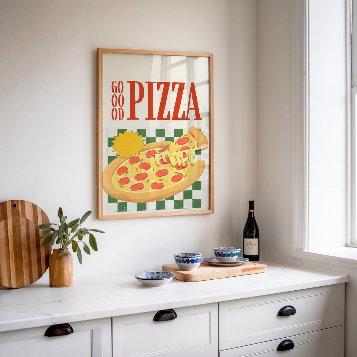 Goood Pizza print in an oak frame above a white sideboard with a bottle of wine