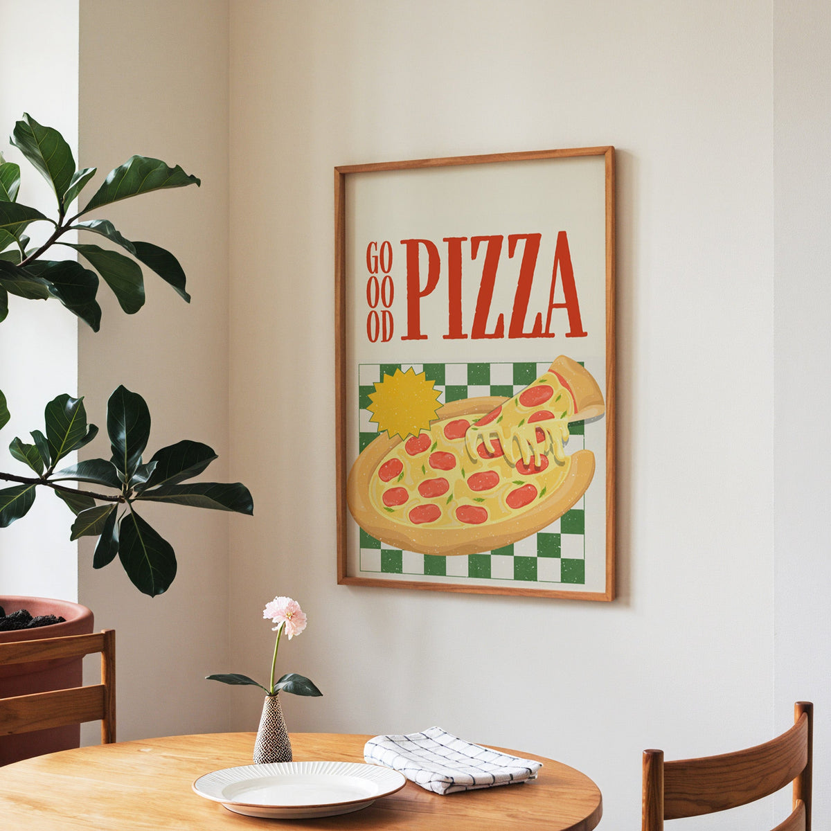 Goood Pizza print in a walnut frame above a round table beside a fiddle-leaf fig
