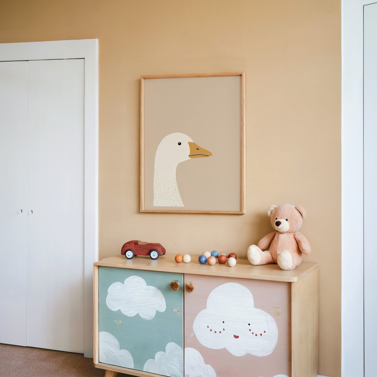 Goose head profile nursery print in an oak frame on a peach wall above a cloud-painted cabinet