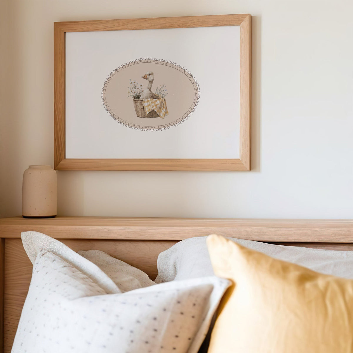 Goose in wicker basket with gingham in lace oval nursery print in an oak frame above a wooden headboard with a mustard pillow