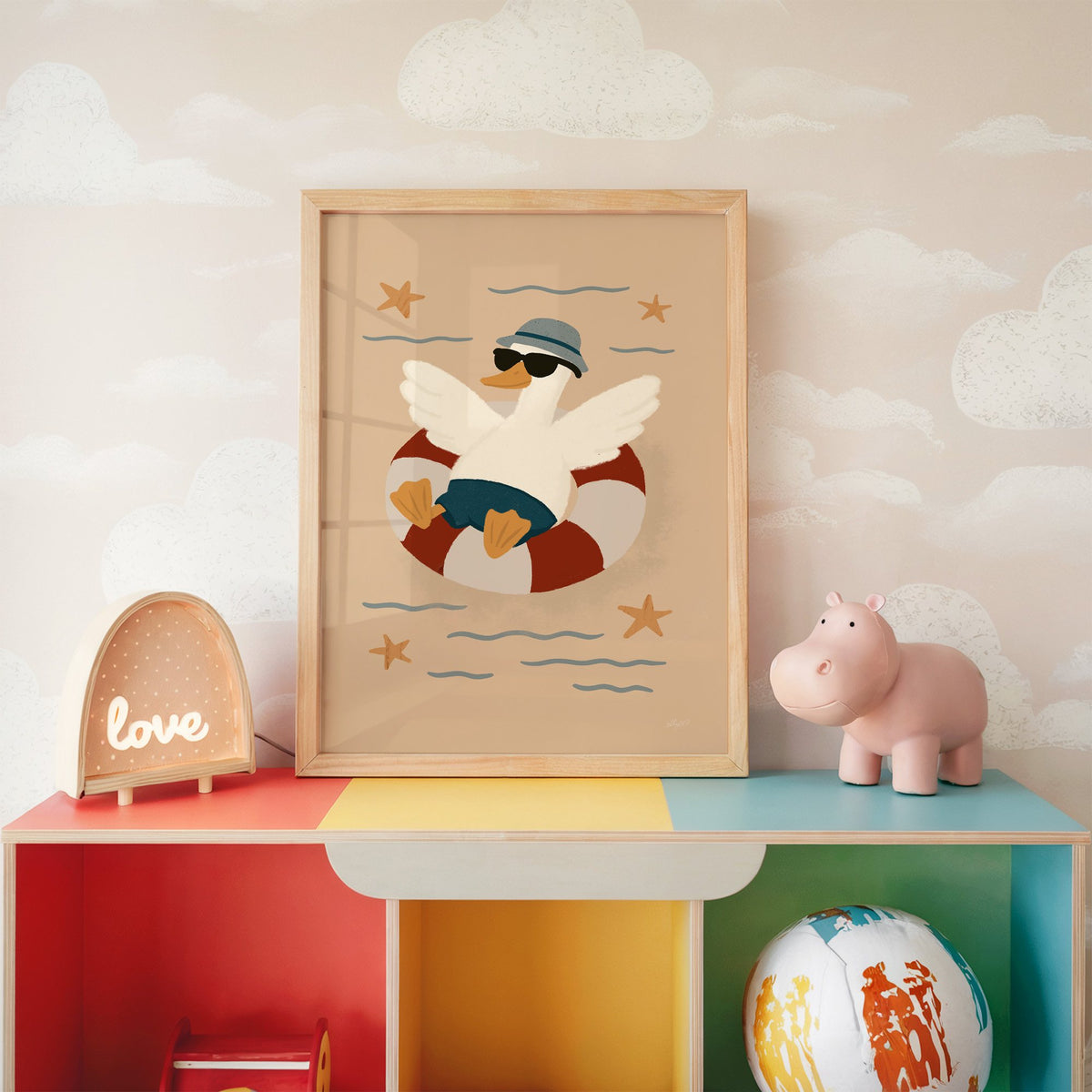 Goose in lifesaver ring nursery print in an oak frame on a rainbow toy shelf against cloud wallpaper