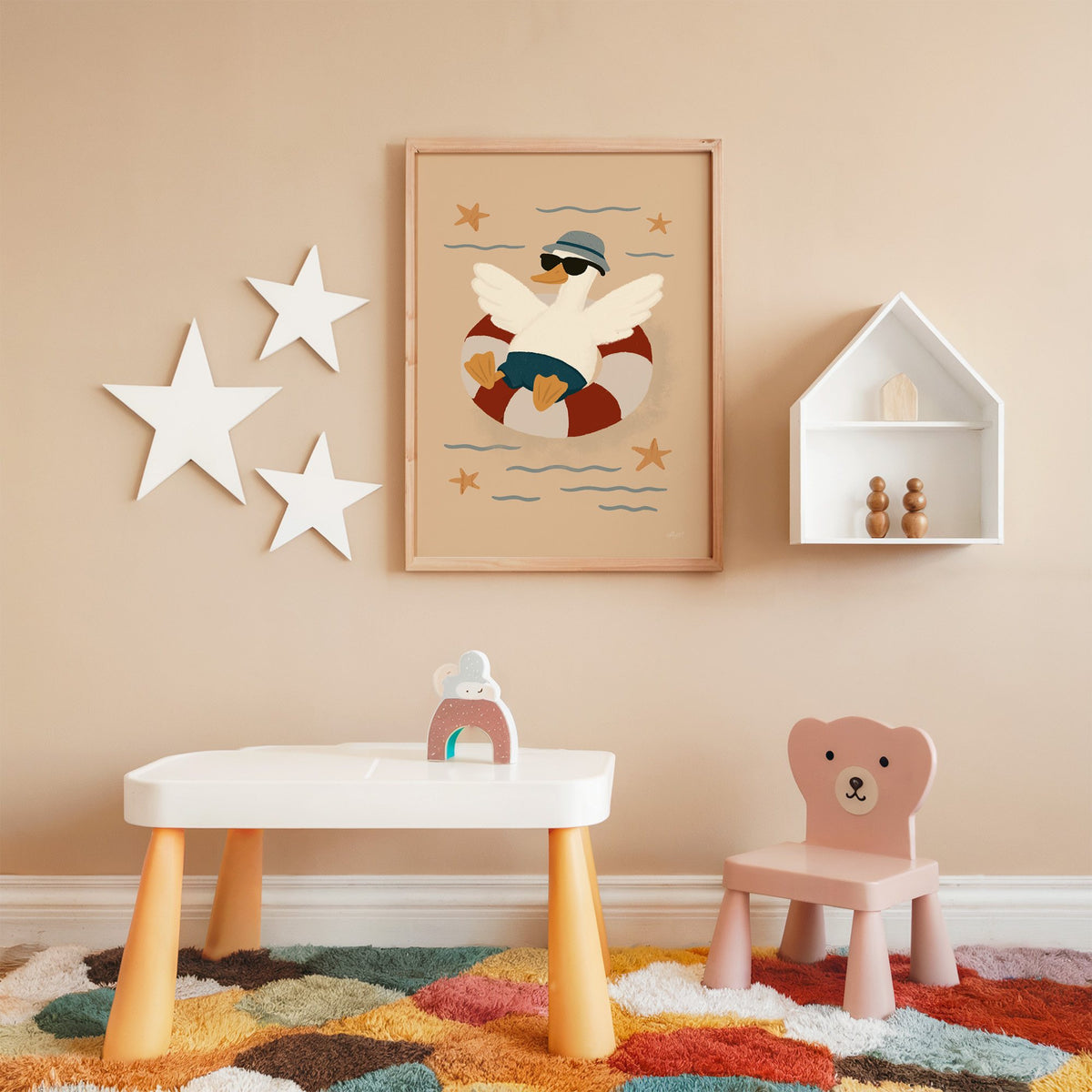 Goose in lifesaver ring nursery print in an oak frame on a peach wall above a kids table with wall stars