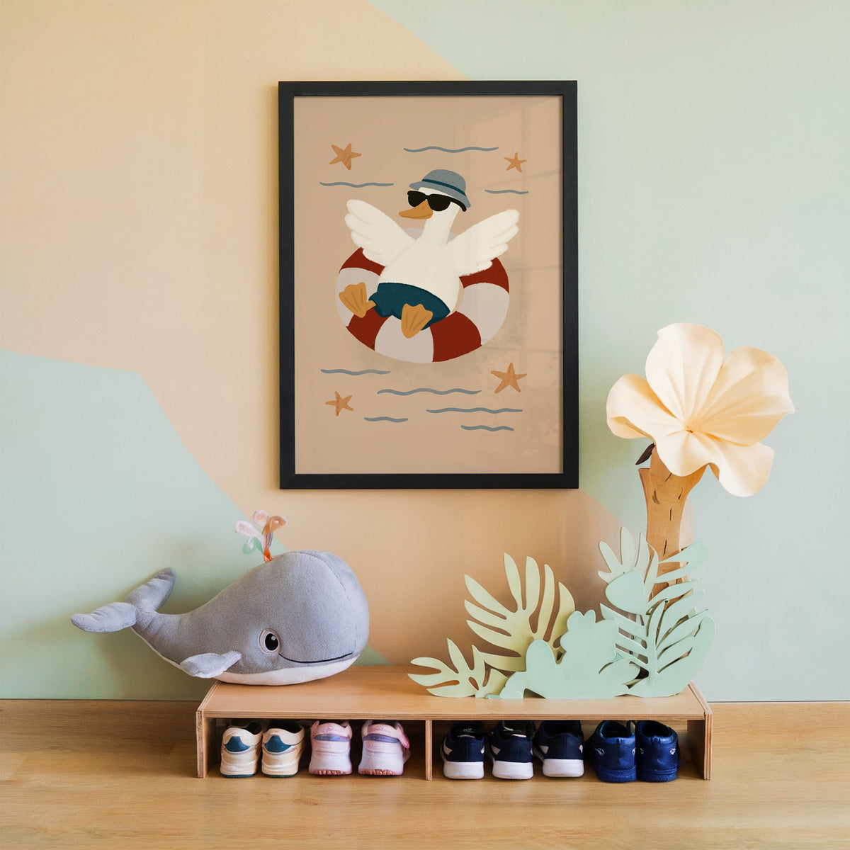 Goose in lifesaver ring nursery print in a black frame on a mint and peach wall above a whale plush
