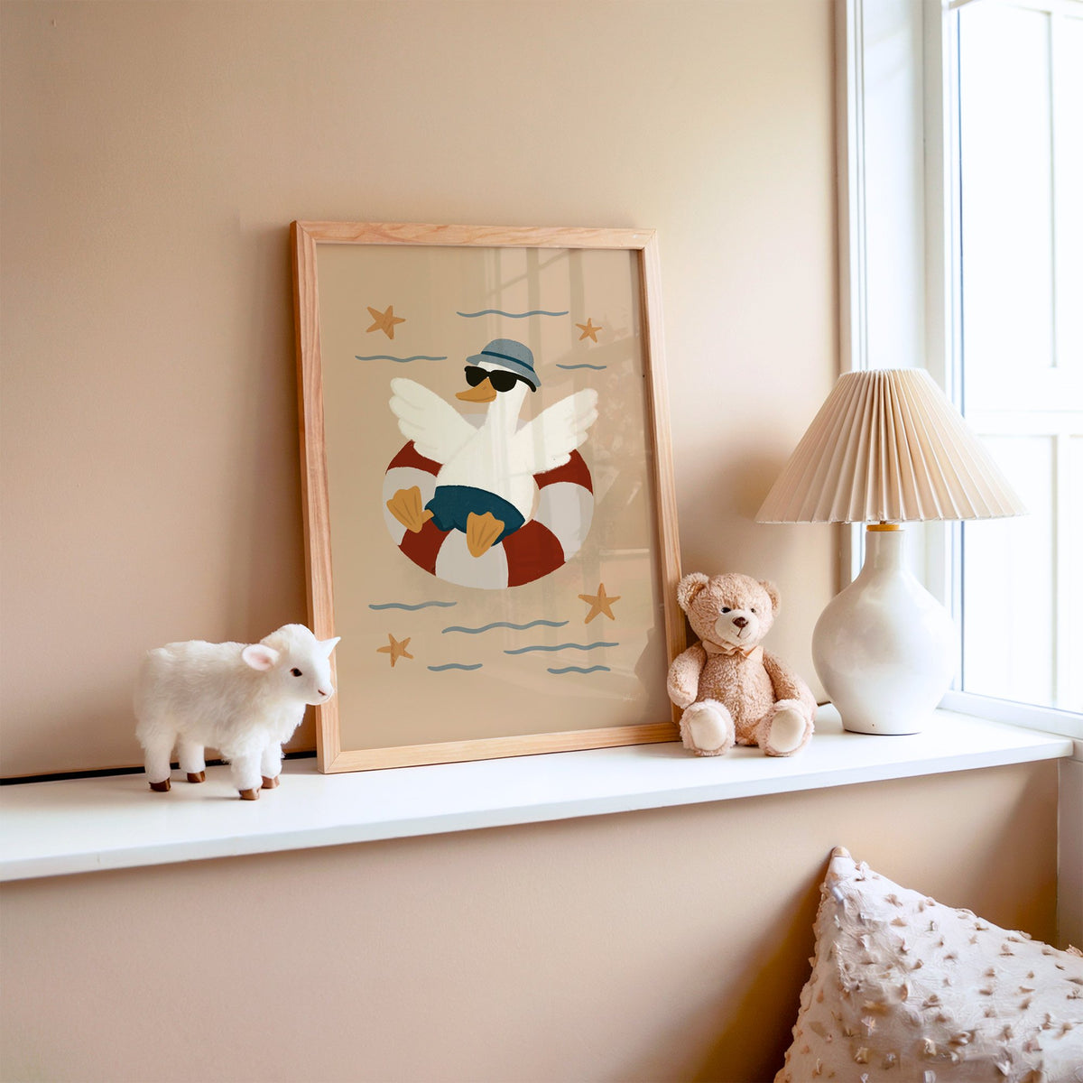 Goose in lifesaver ring nursery print in an oak frame on a window ledge with a toy lamb and teddy