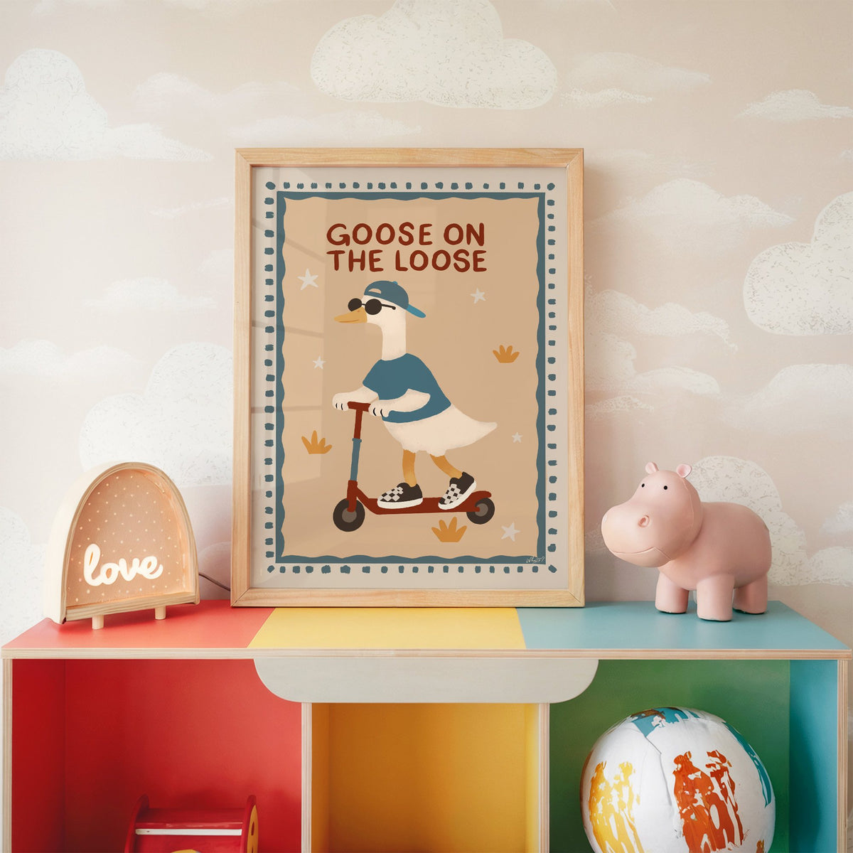 Goose on the loose scooter nursery print in an oak frame on a rainbow toy shelf against cloud wallpaper