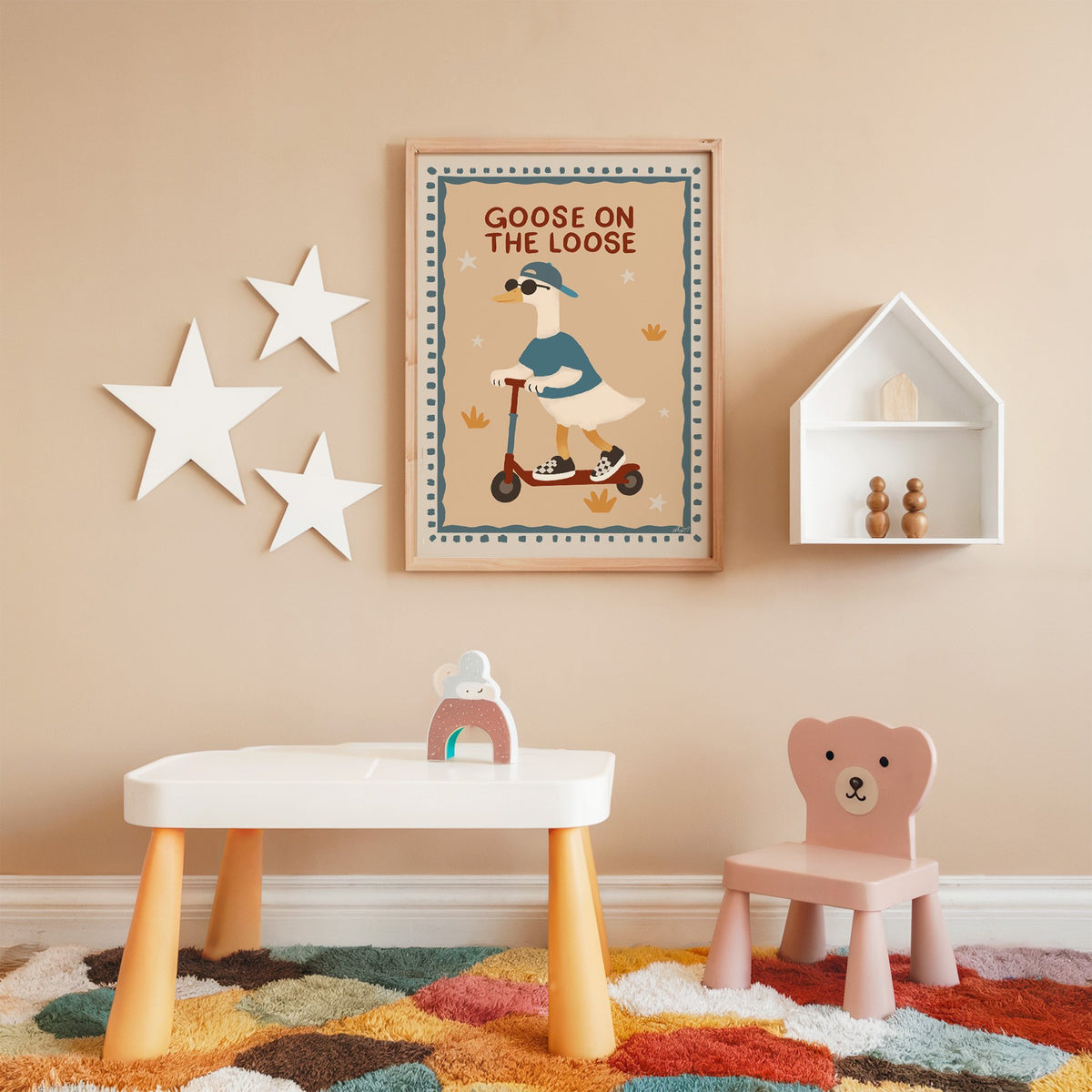 Goose on the loose scooter nursery print in an oak frame on a peach wall above a kids table with wall stars