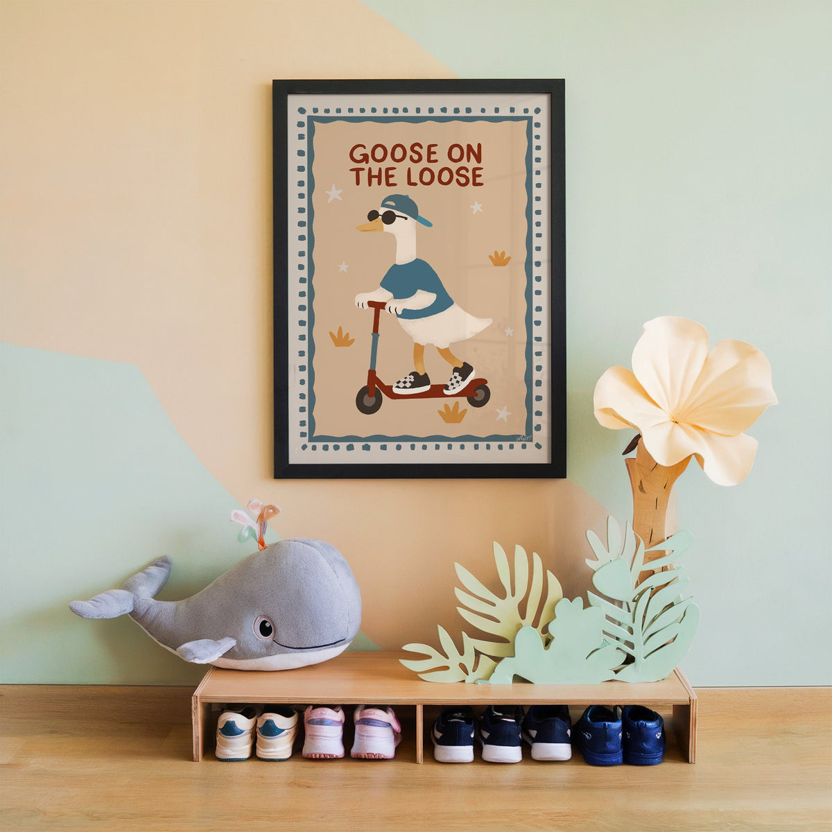 Goose on the loose scooter nursery print in a black frame on a mint and peach wall above a whale plush
