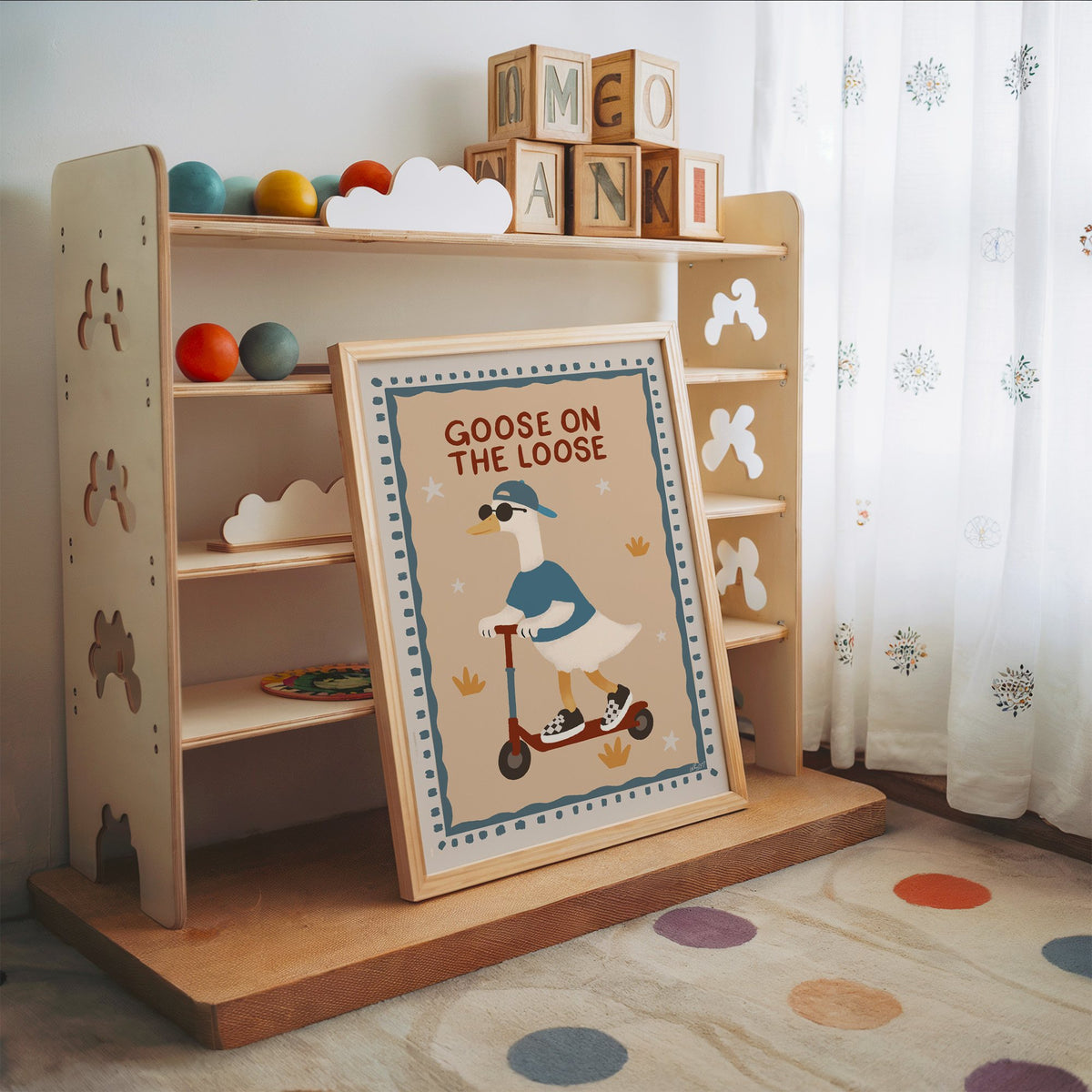 Goose on the loose scooter nursery print in an oak frame leaning on a toy shelf with wooden letter blocks