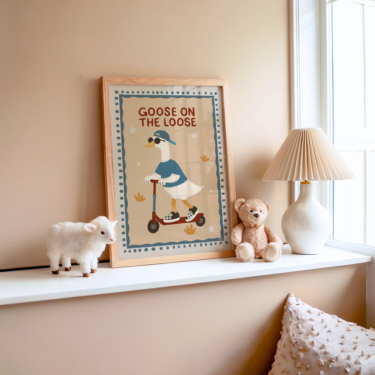 Goose on the loose scooter nursery print in an oak frame on a window ledge with a toy lamb and teddy