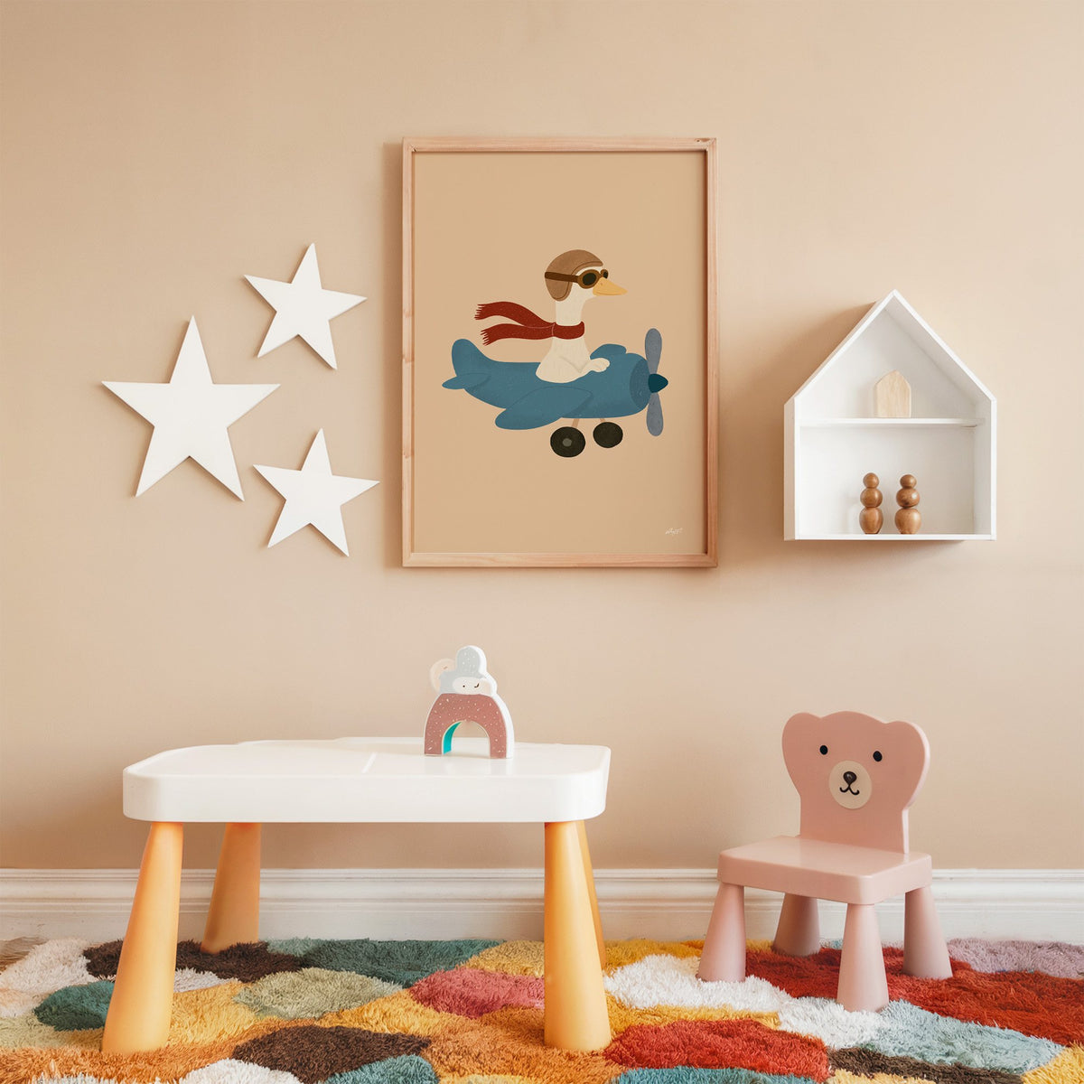 Goose pilot in blue airplane nursery print in an oak frame on a peach wall above a kids table with wall stars