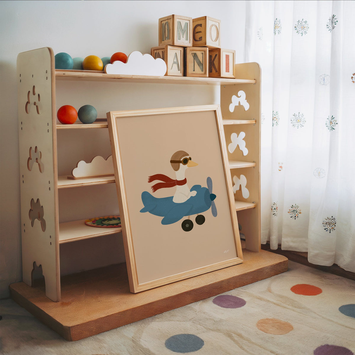 Goose pilot in blue airplane nursery print in an oak frame leaning on a toy shelf with wooden letter blocks