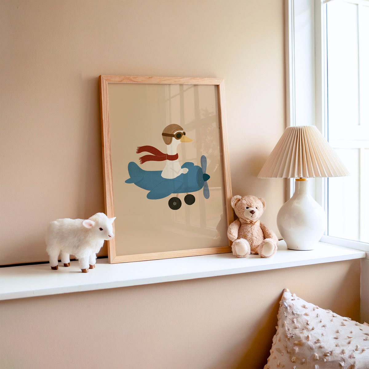 Goose pilot in blue airplane nursery print in an oak frame on a window ledge with a toy lamb and teddy