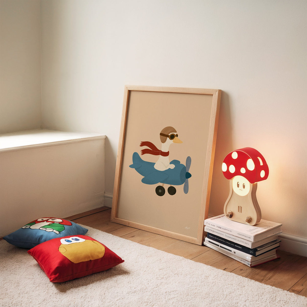 Goose pilot in blue airplane nursery print in an oak frame leaning on a rug beside a mushroom lamp and floor cushions
