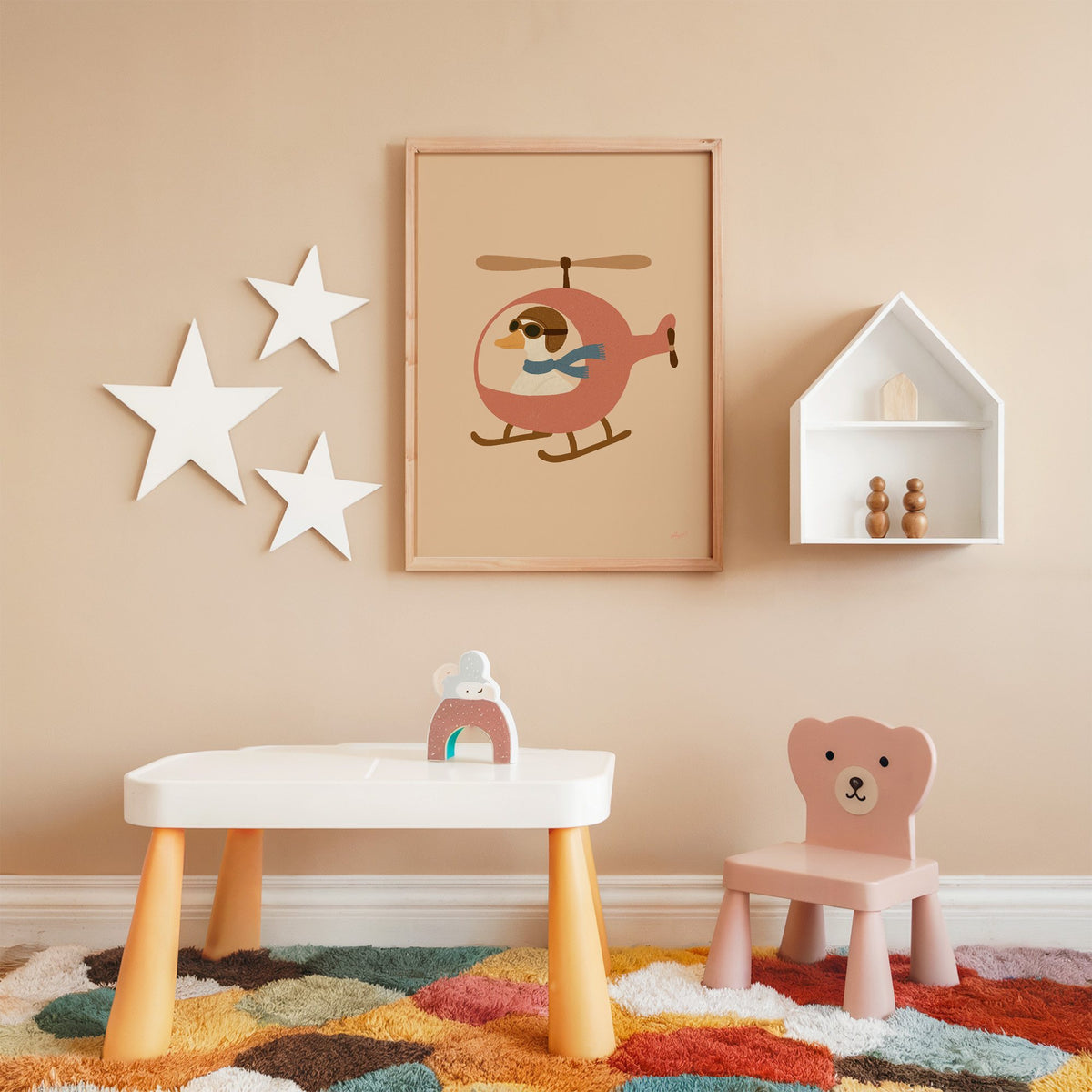 Goose pilot in pink helicopter nursery print in an oak frame on a peach wall above a kids table with wall stars