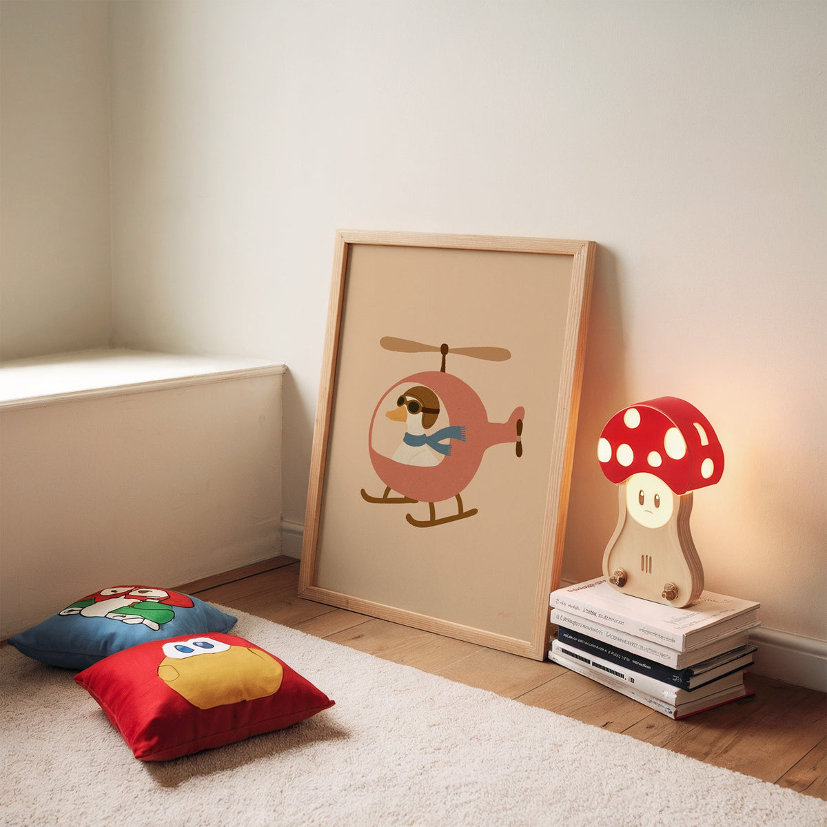 Goose pilot in pink helicopter nursery print in an oak frame leaning on a rug beside a mushroom lamp and floor cushions