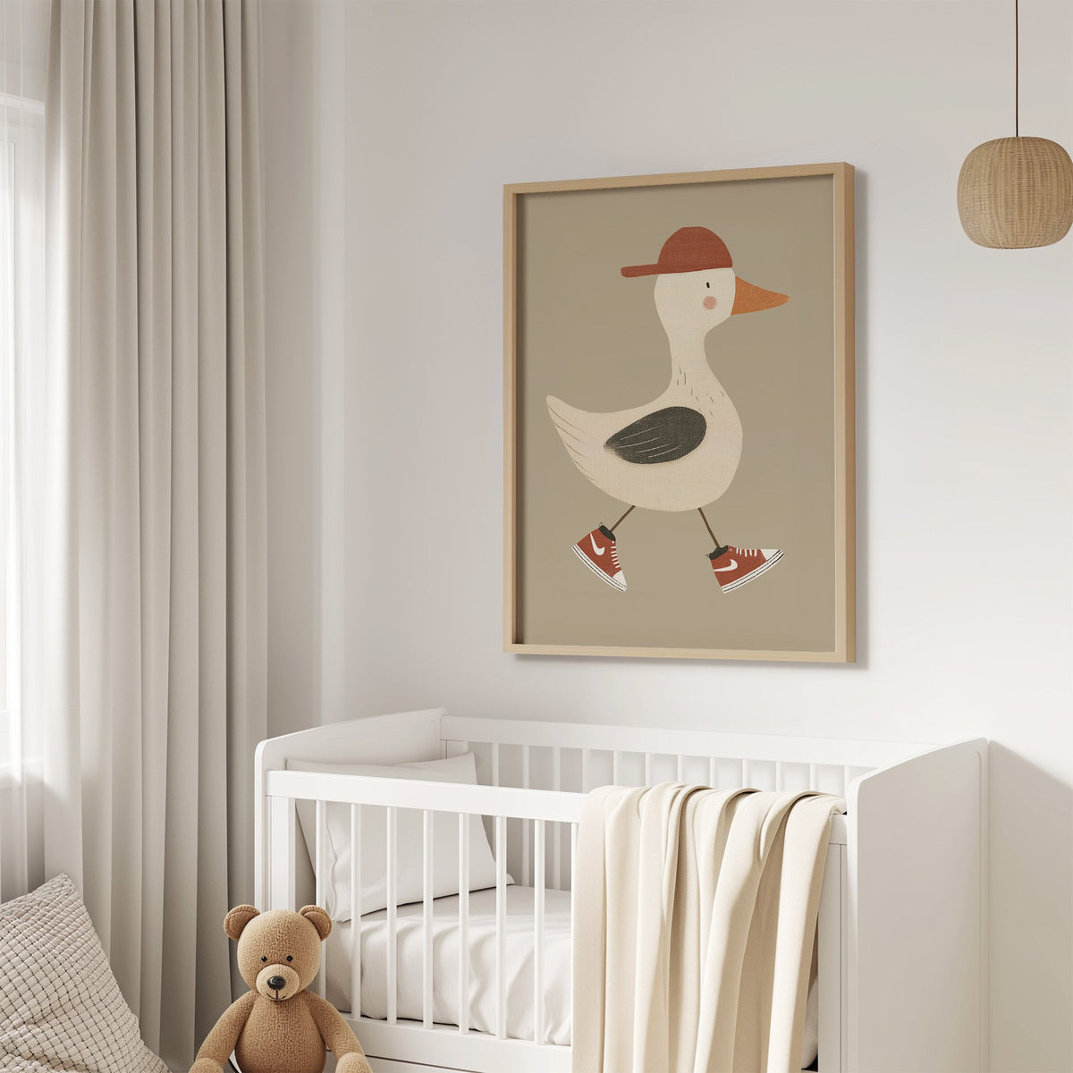 Goose red cap and sneakers nursery print in an oak frame above a white crib with a teddy bear
