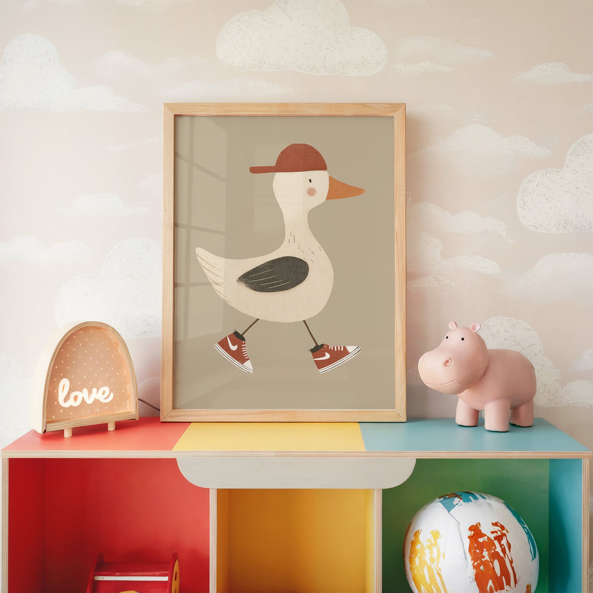 Goose red cap and sneakers nursery print in an oak frame on a rainbow toy shelf against cloud wallpaper