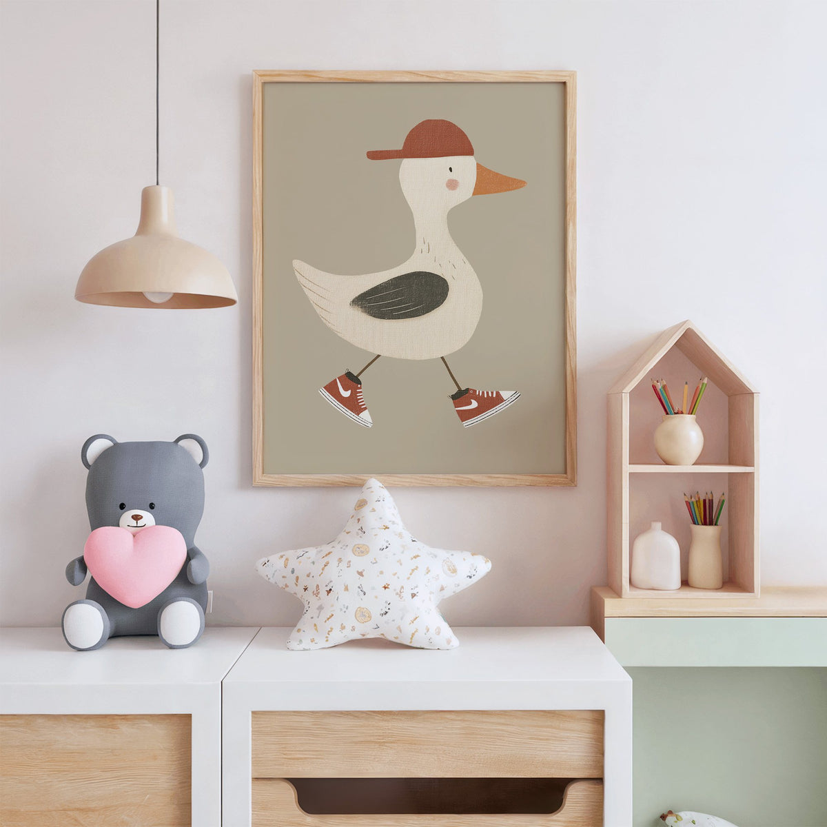 Goose red cap and sneakers nursery print in an oak frame above a white dresser with a star pillow and house shelf