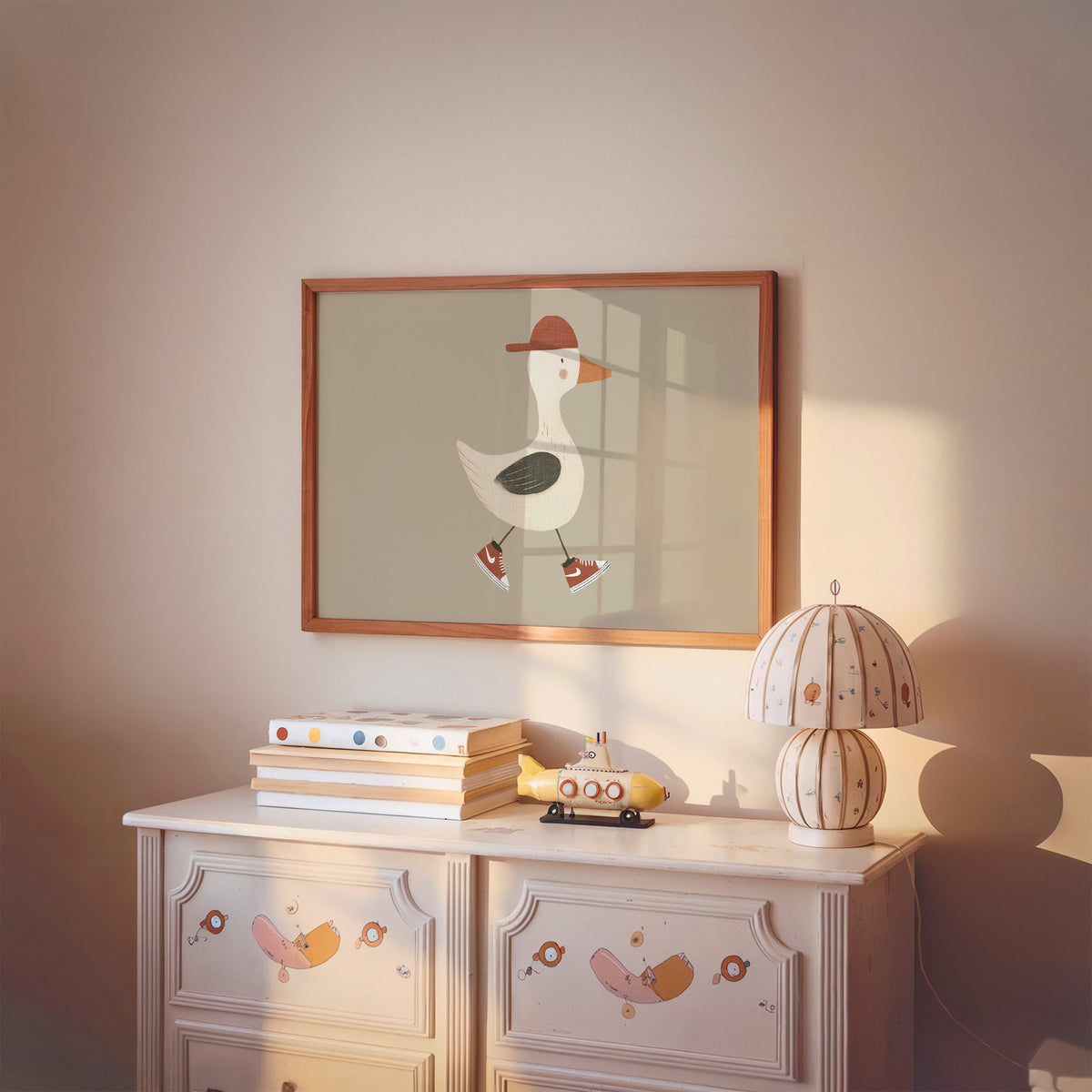 Landscape goose red cap and sneakers nursery print in a cherry wood frame above a painted dresser and lamp