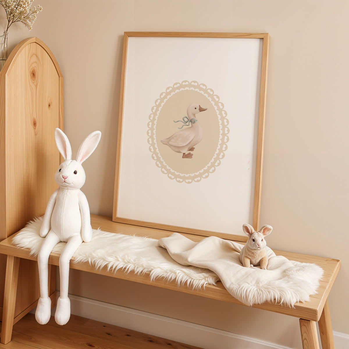 Goose with sage ribbon in heart lace oval nursery print in an oak frame on a sheepskin bench beside a white plush bunny