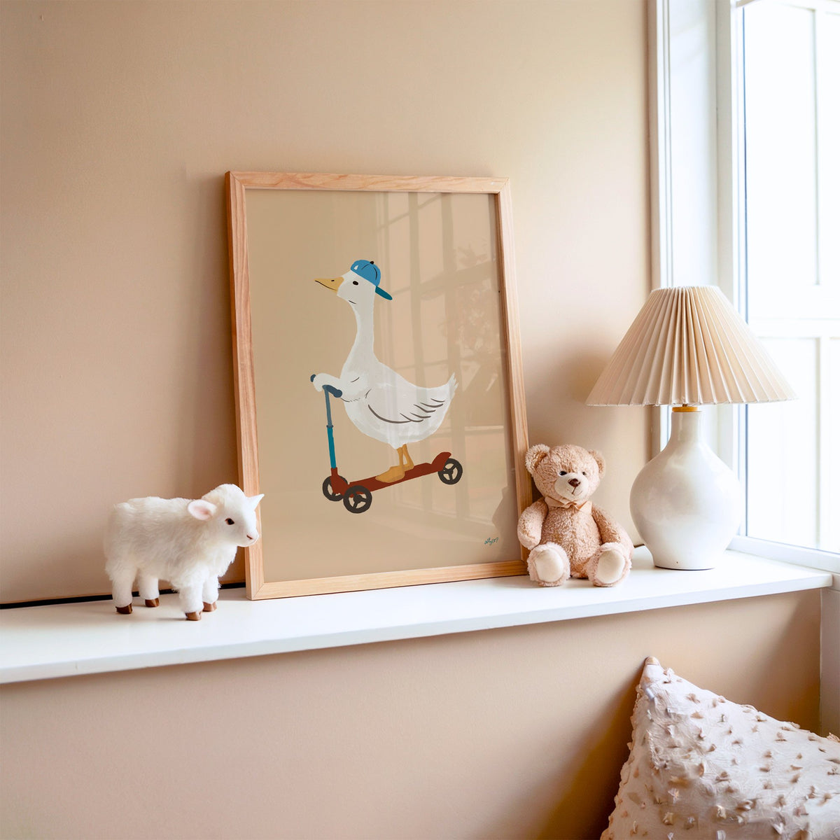 Goose riding scooter in blue cap nursery print in an oak frame on a window ledge with a toy lamb and teddy