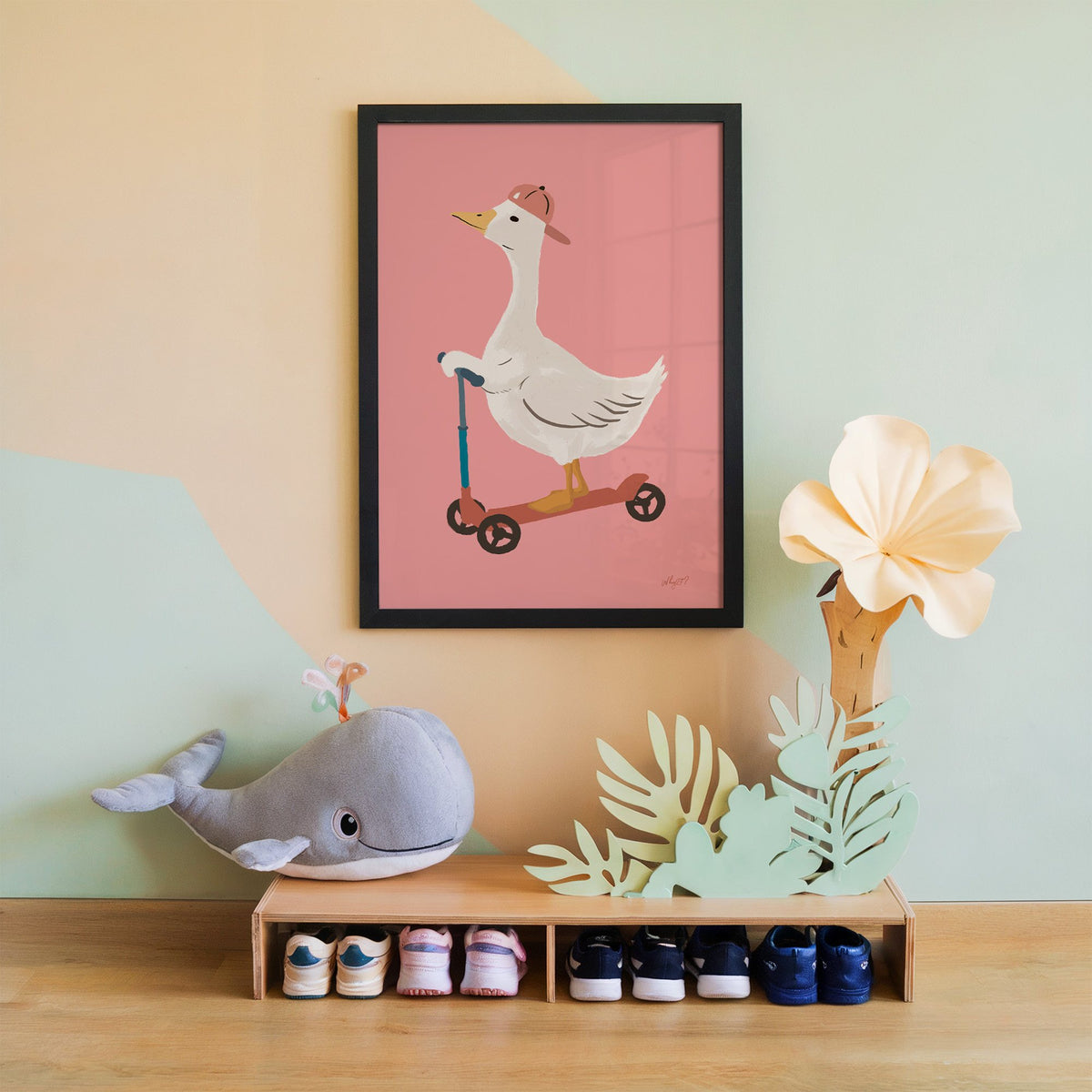 Goose on scooter in pink cap nursery print in a black frame on a mint and peach wall above a whale plush