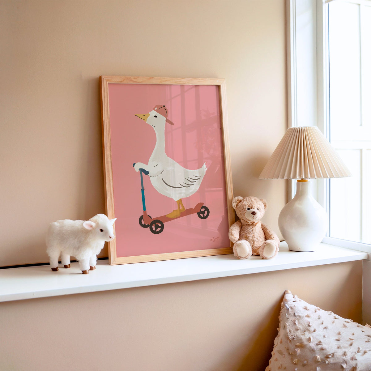 Goose on scooter in pink cap nursery print in an oak frame on a window ledge with a toy lamb and teddy