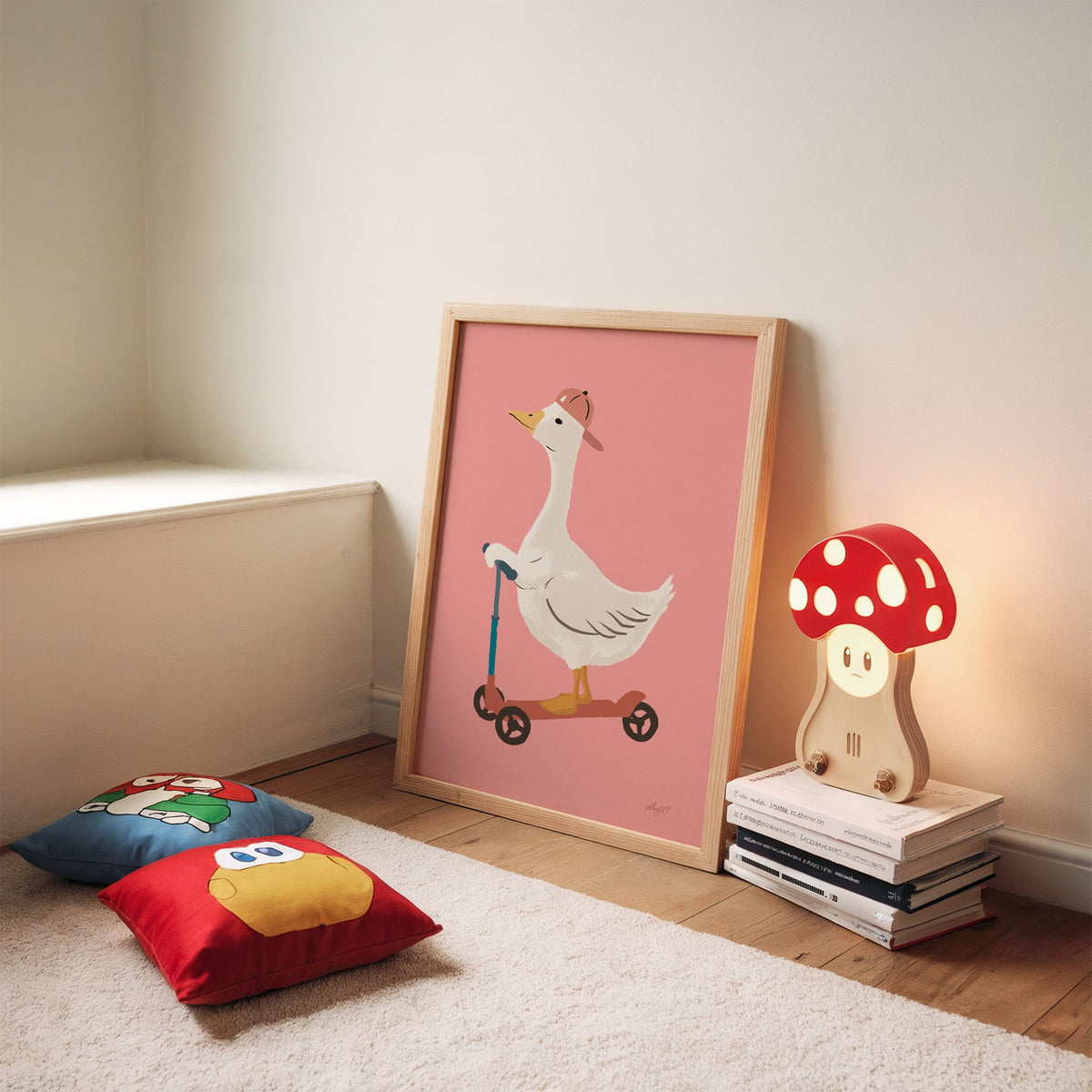 Goose on scooter in pink cap nursery print in an oak frame leaning on a rug beside a mushroom lamp and floor cushions