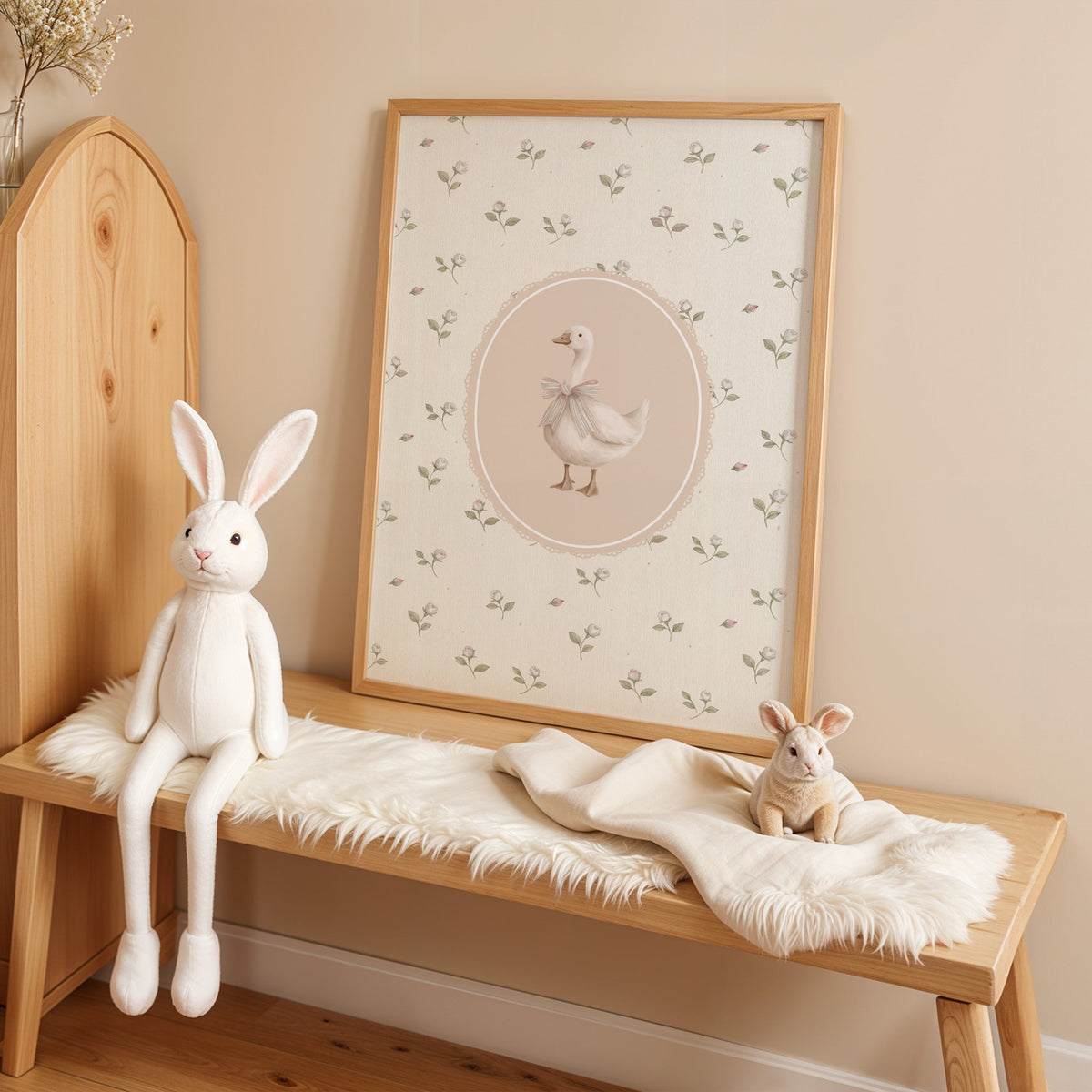 White goose with striped bow in lace oval nursery print in an oak frame on a sheepskin bench beside a white plush bunny
