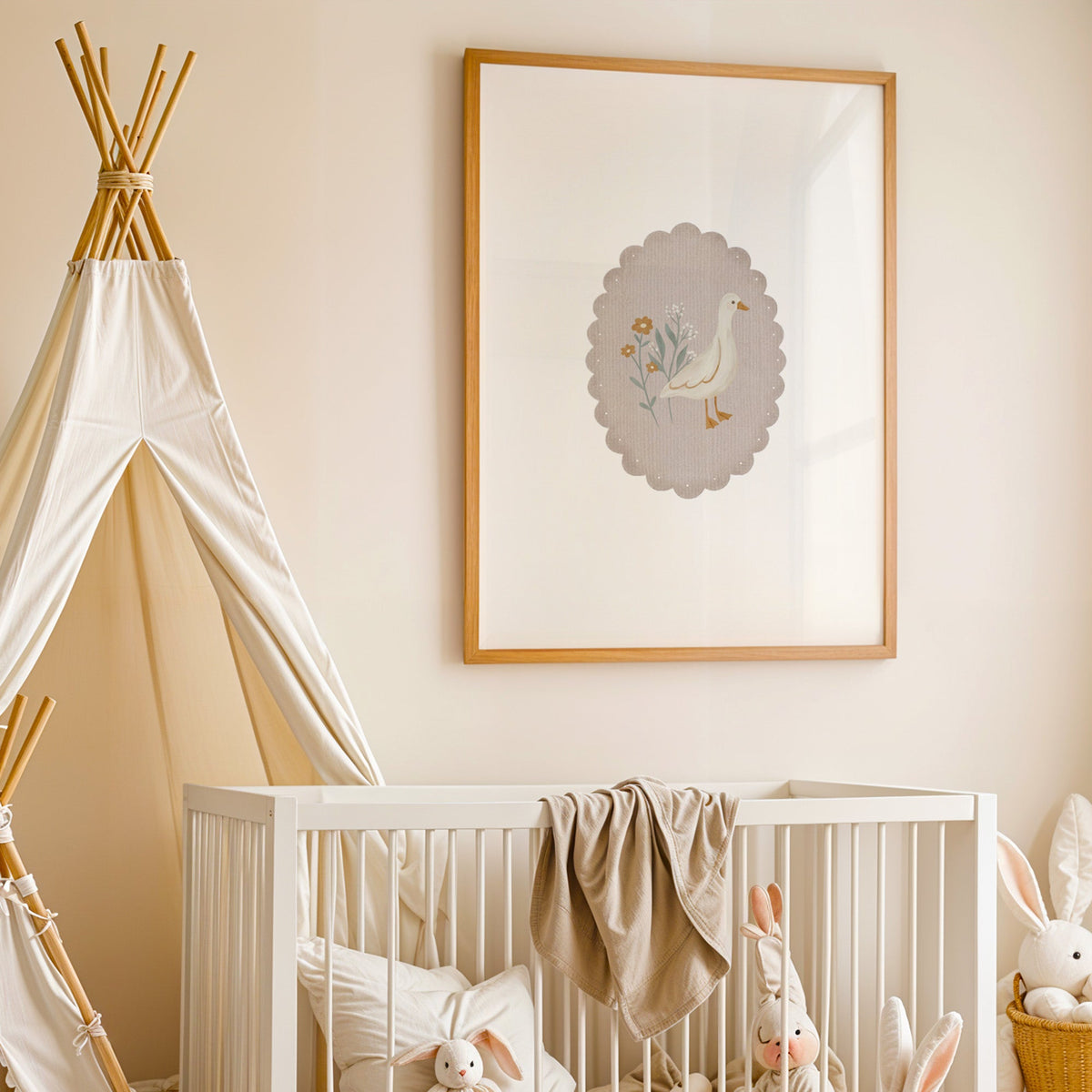 White goose and wildflowers in scalloped oval nursery print in an oak frame above a white crib beside a canvas teepee
