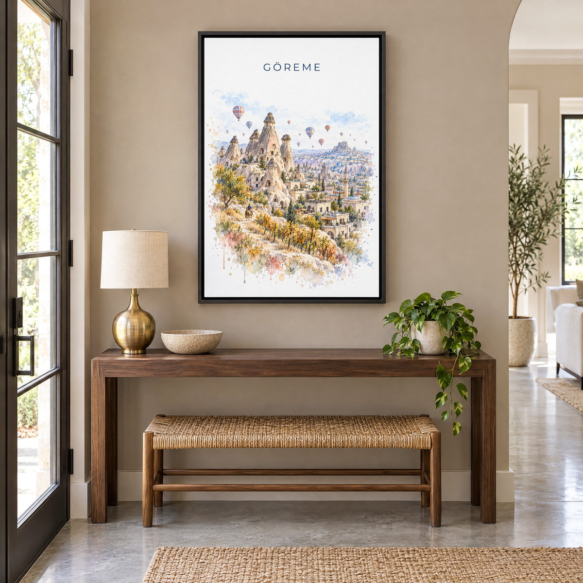 Göreme watercolor print as a black floater canvas above a walnut console and woven bench in an entryway