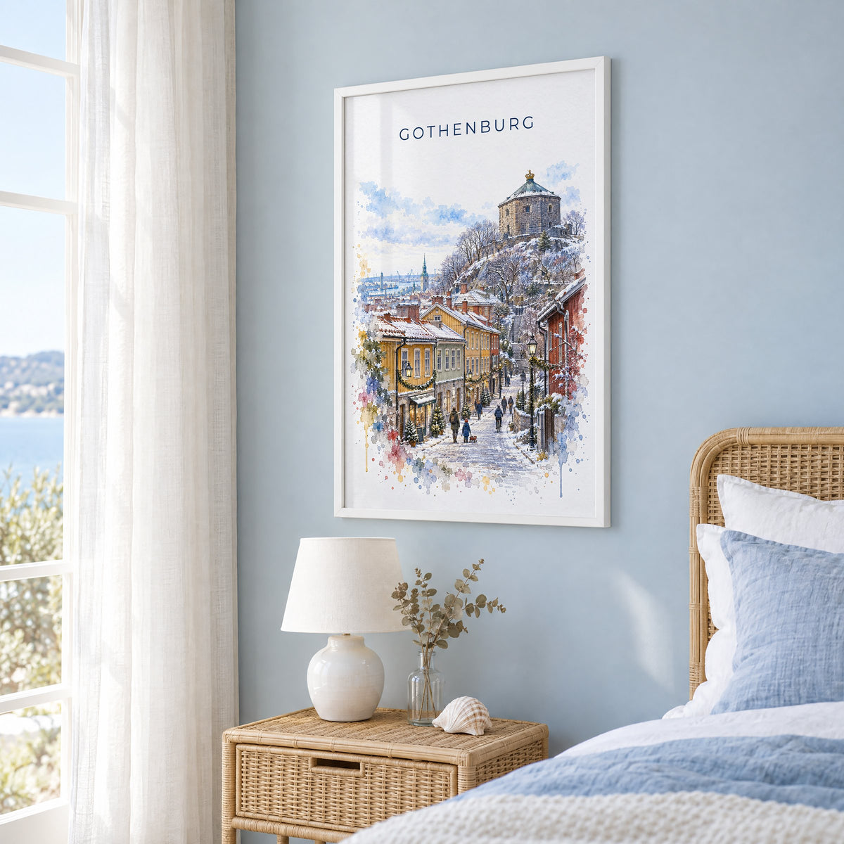 Gothenburg watercolor print in a white frame on a pale blue wall beside a rattan bed in a coastal bedroom