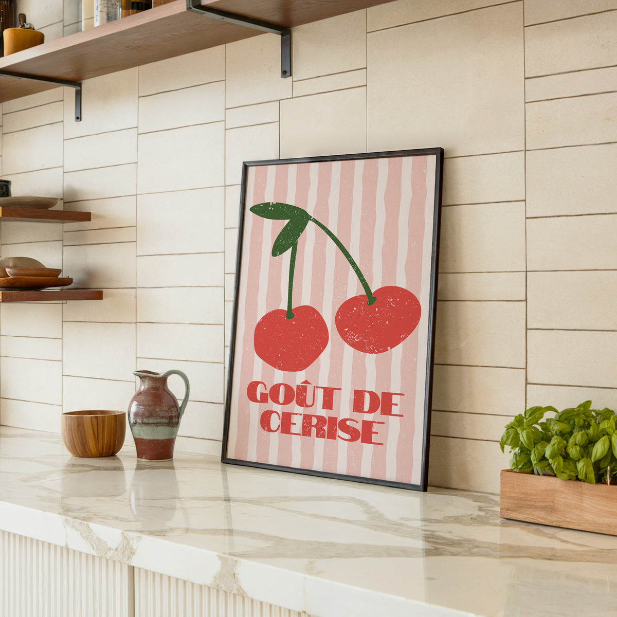 Gout de Cerise cherry print in a black frame leaning on a marble counter in a tiled kitchen