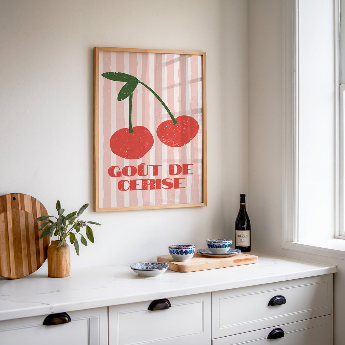Gout de Cerise cherry print in an oak frame above a white sideboard with a bottle of wine