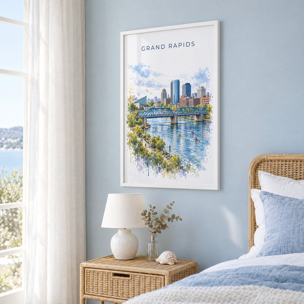 Grand Rapids watercolor print in a white frame on a pale blue wall beside a rattan bed in a coastal bedroom