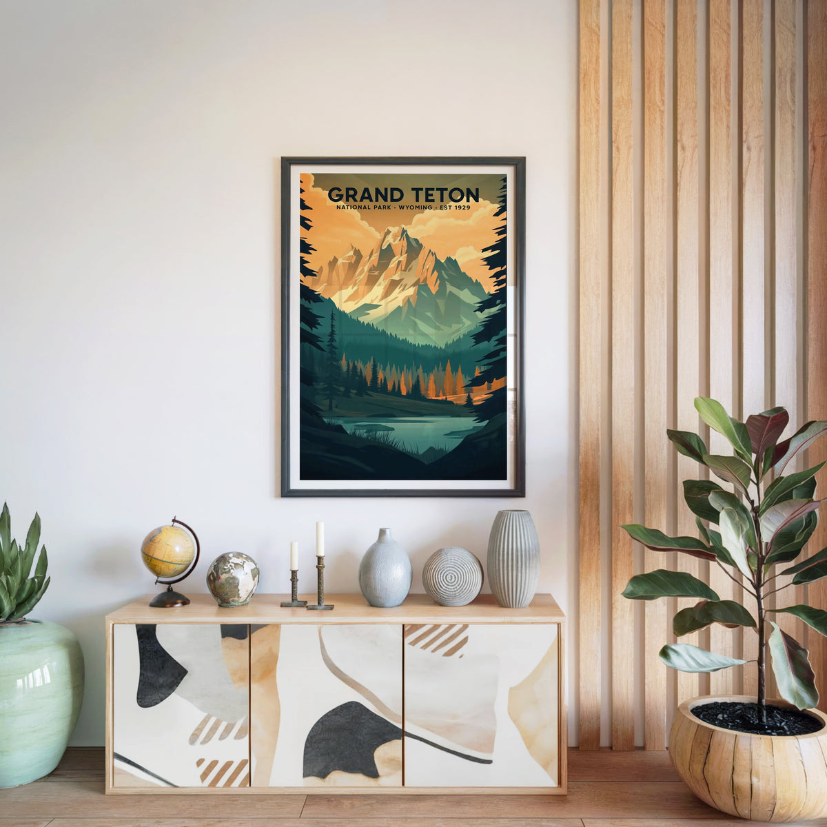 Grand Teton National Park print in a black frame above a light wood sideboard with a globe and vases