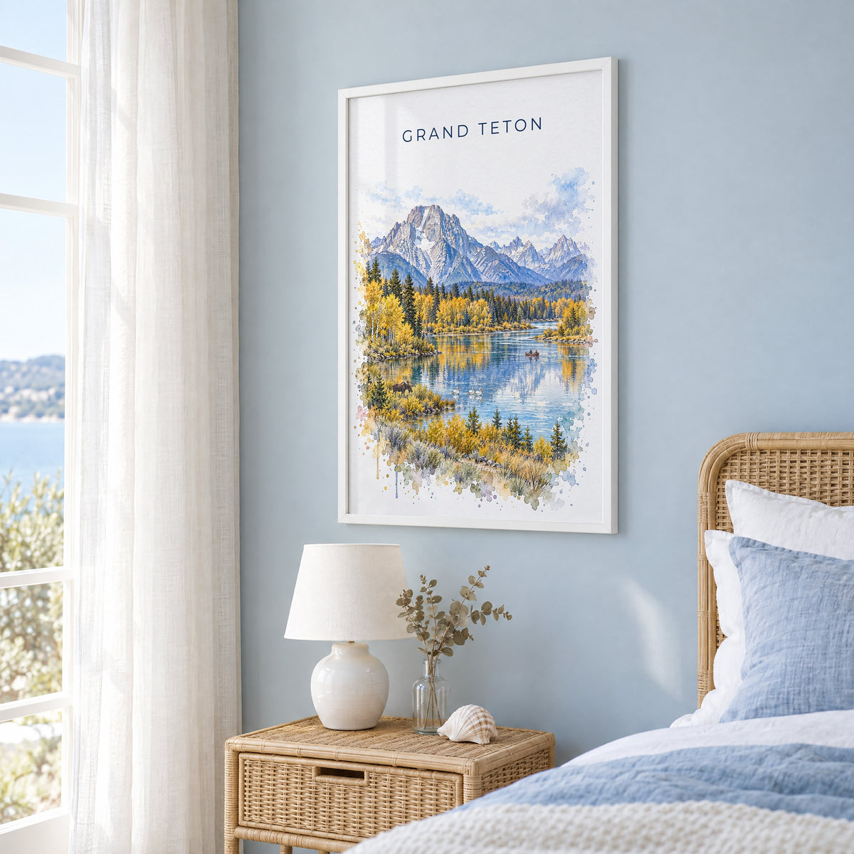 Grand Teton National Park watercolor print in a white frame on a pale blue wall beside a rattan bed in a coastal bedroom
