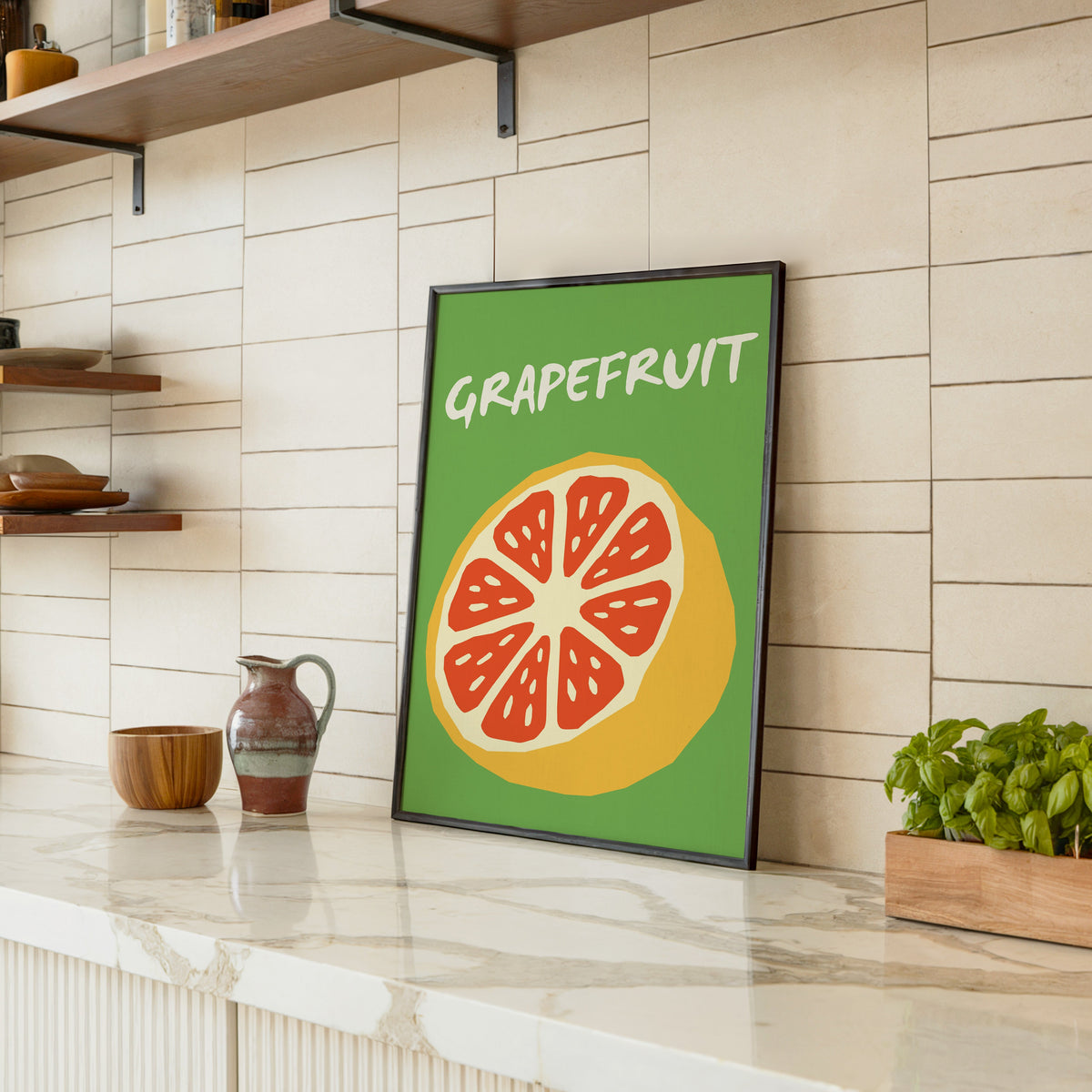 Grapefruit half print in a black frame leaning on a marble counter in a tiled kitchen