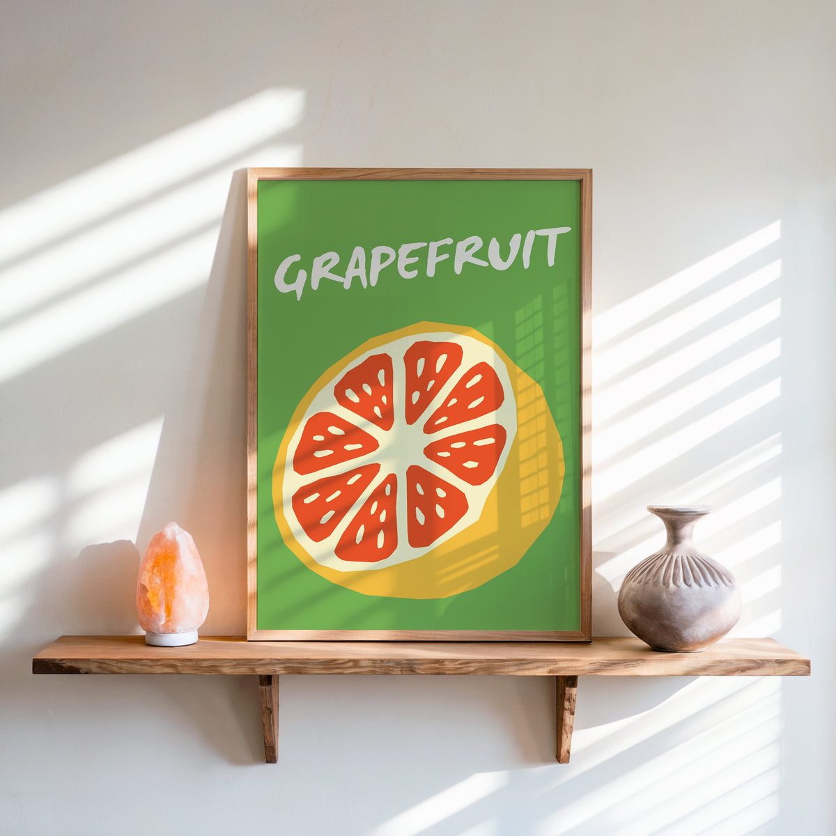 Grapefruit half print in an oak frame on a live-edge shelf beside a salt lamp