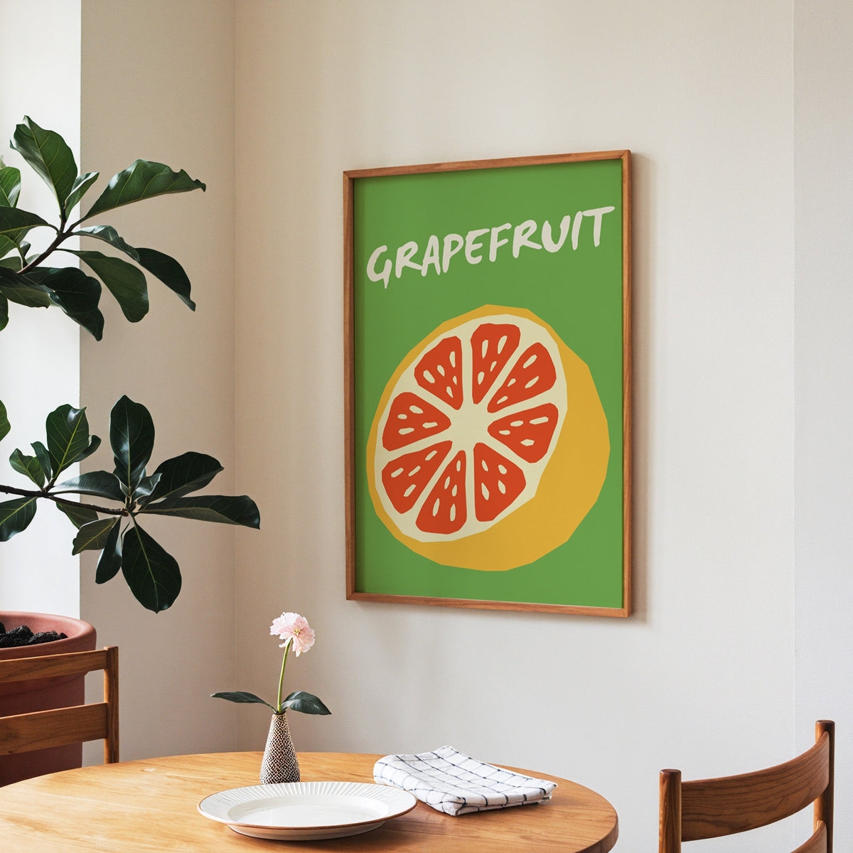 Grapefruit half print in a walnut frame above a round table beside a fiddle-leaf fig
