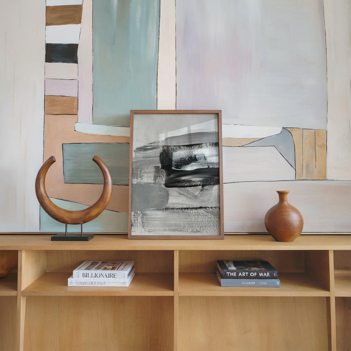 Gray and black dry brush layers abstract print in a walnut frame on an oak shelf beside a wooden crescent sculpture