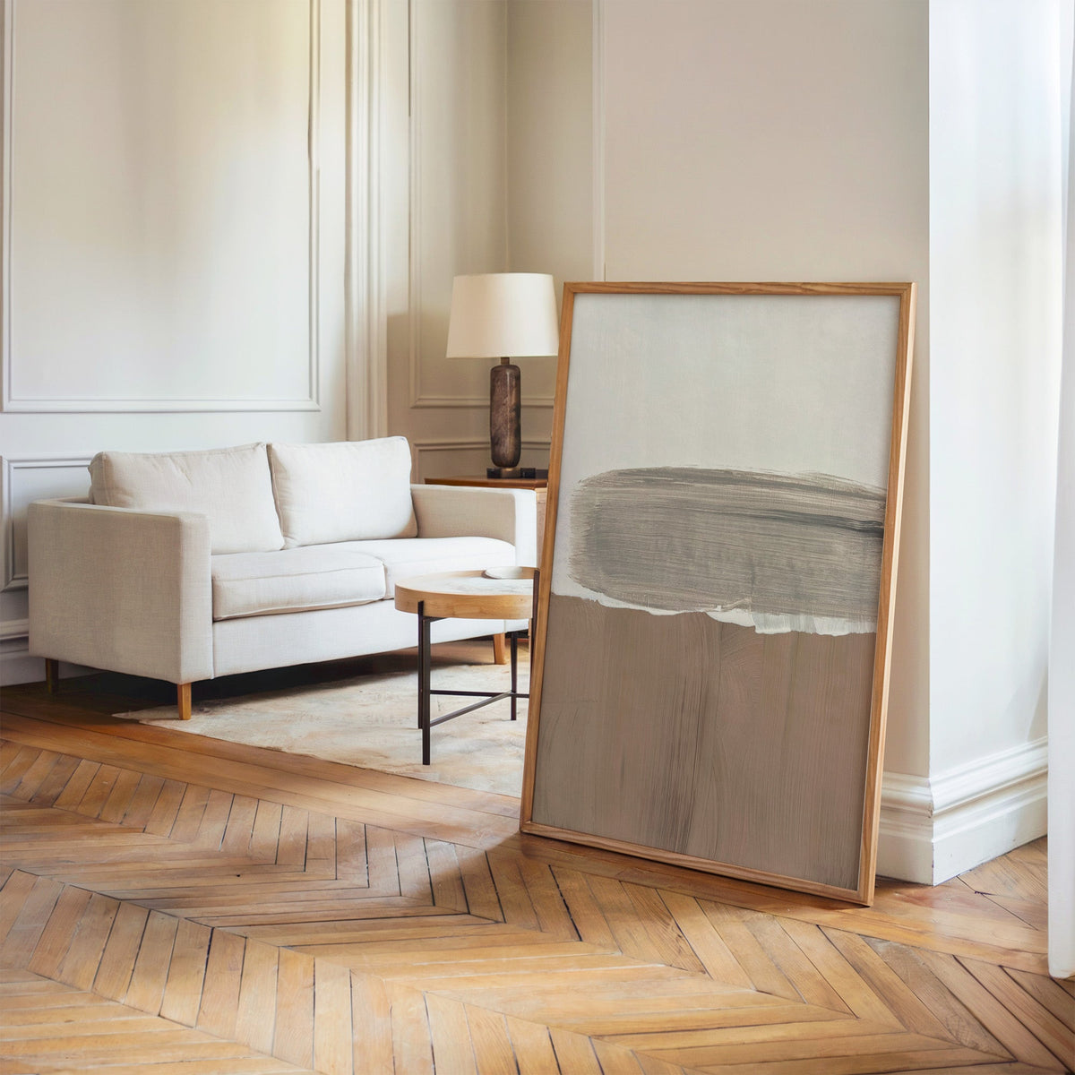 Gray brush band over mocha brushstroke print in an oak frame leaning on a herringbone floor by a cream linen sofa