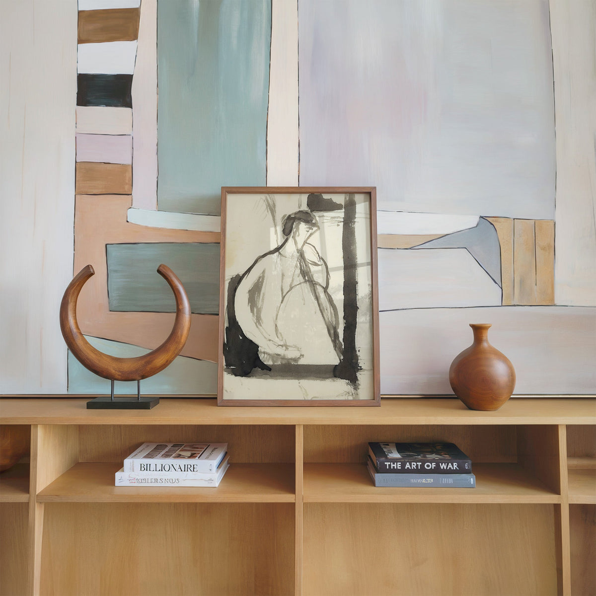 Gray ink seated woman figure sketch print in a walnut frame on an oak shelf beside a wooden crescent sculpture