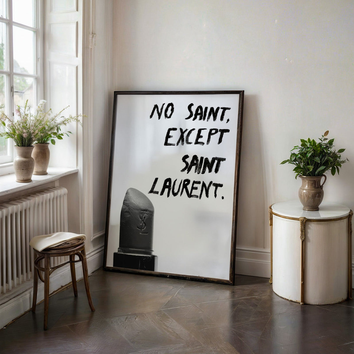 Gray lipstick with black brush lettering quote print in a black frame on a dark stone floor beside a white side table