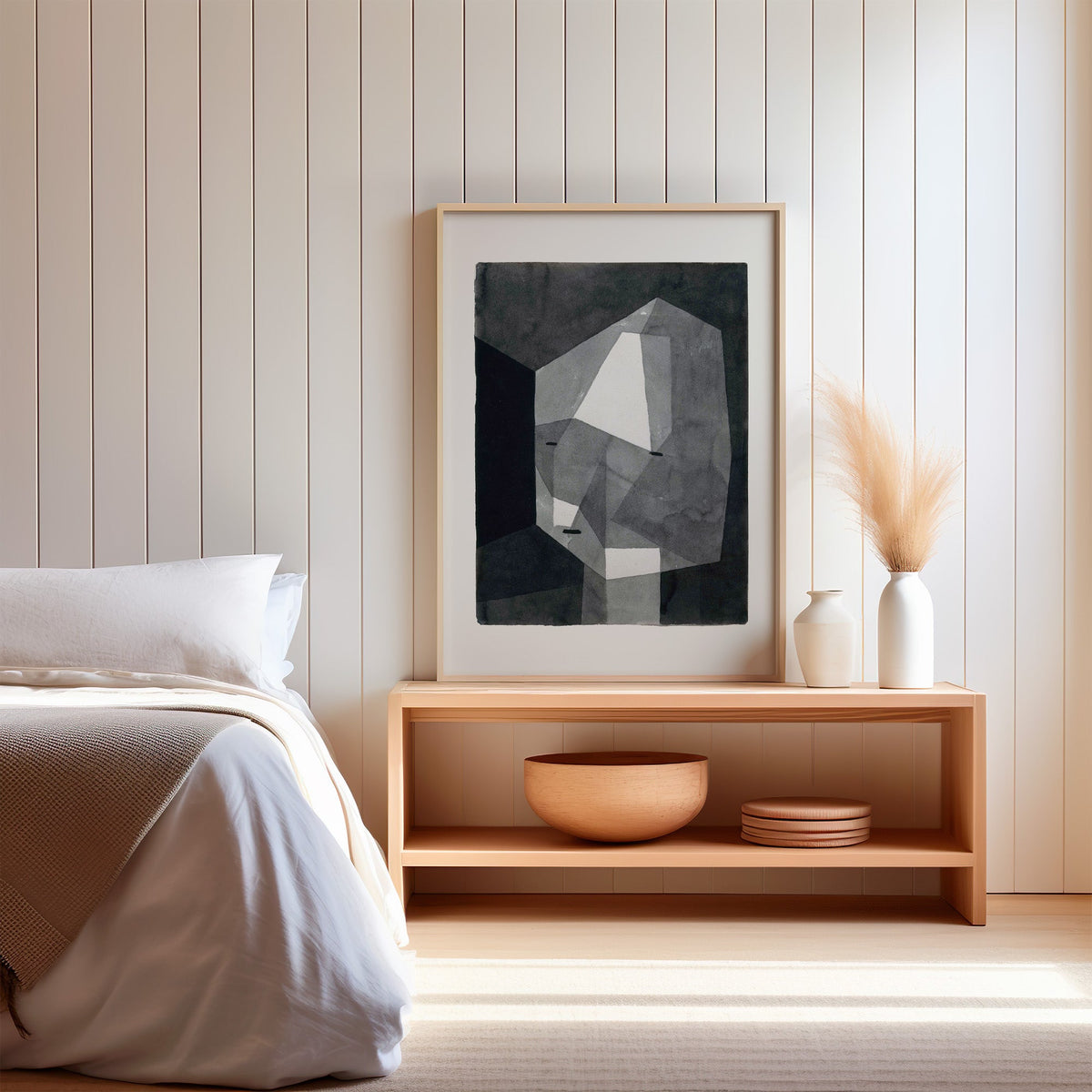 Gray faceted crystal head watercolor abstract print in a light oak frame on a wood bench by a bed with pampas grass